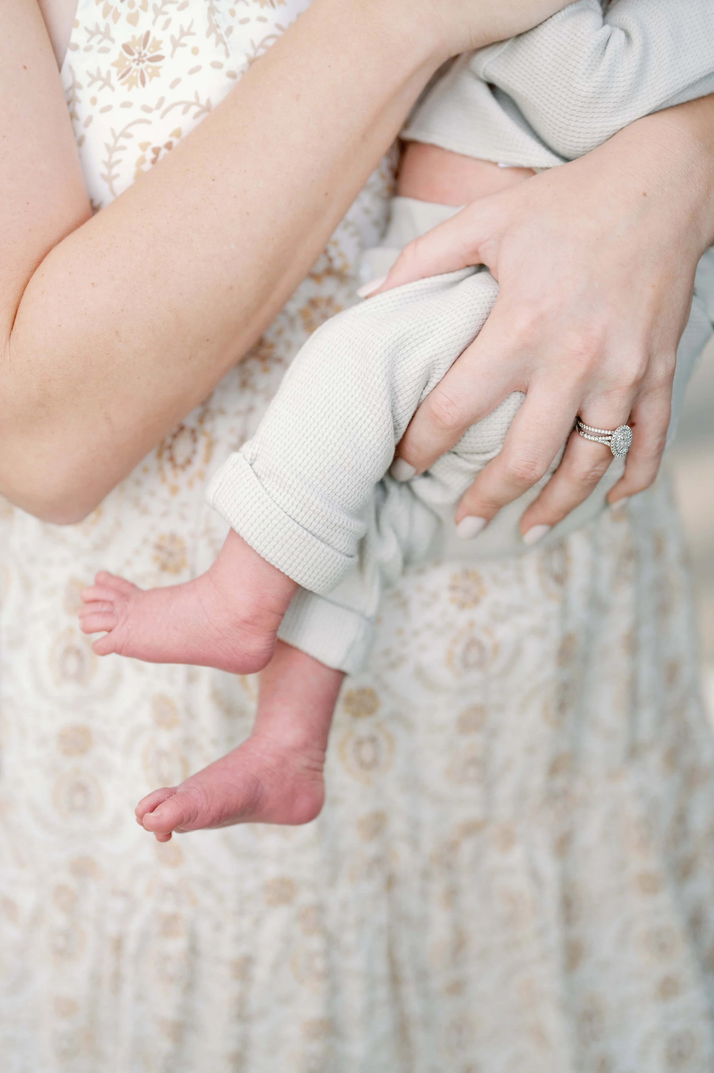 Close-up of a woman holding a baby, focusing on the baby's legs and the woman's hand with a wedding ring.