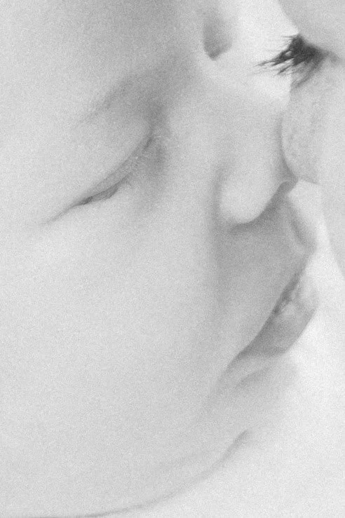 Close-up of a person's face in profile, with closed eyes and slightly parted lips, monochrome image.