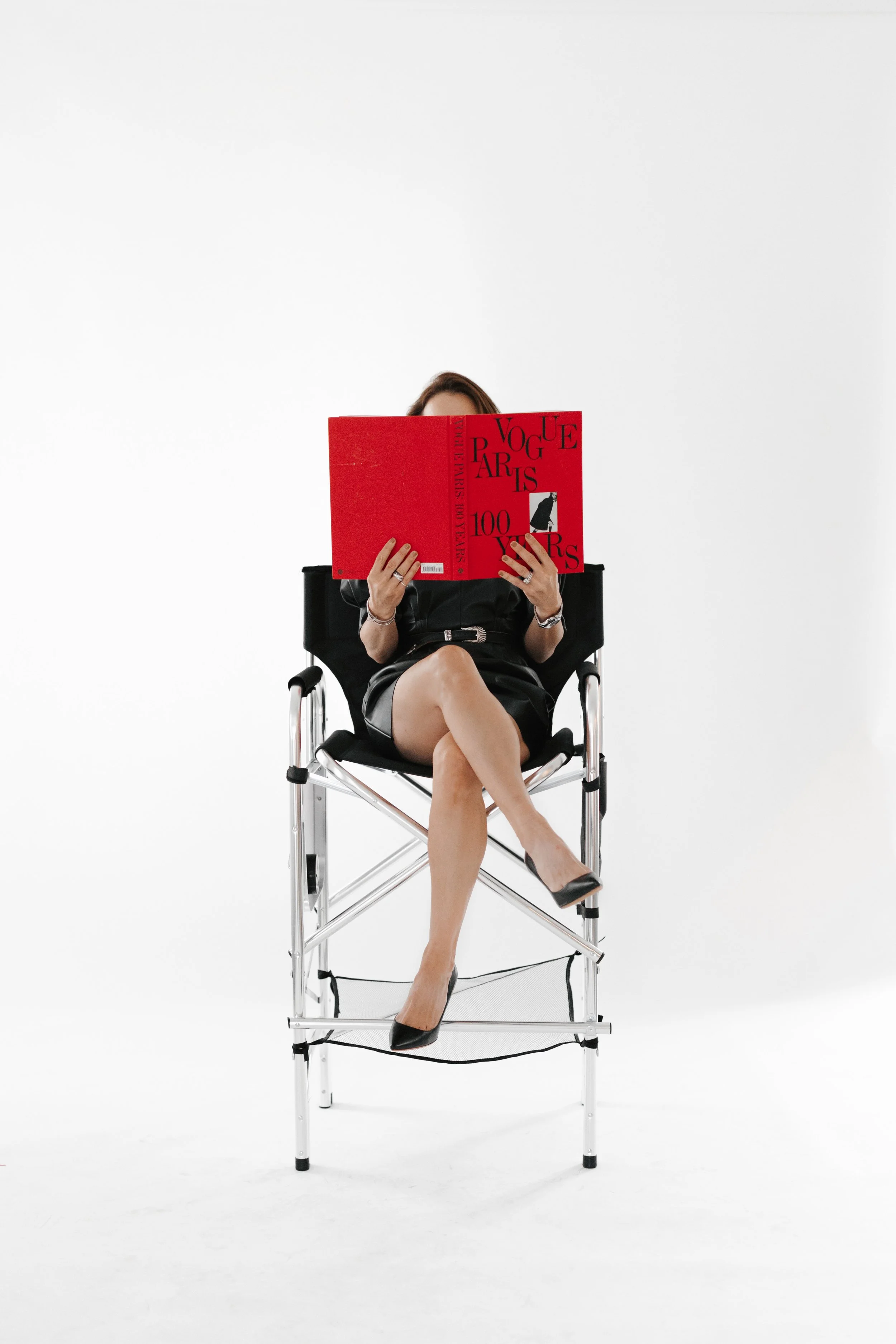 Luxurious woman sitting in a chair reading a bright red Vogue Paris book. DistriktF Park City Photo Studio Rental.