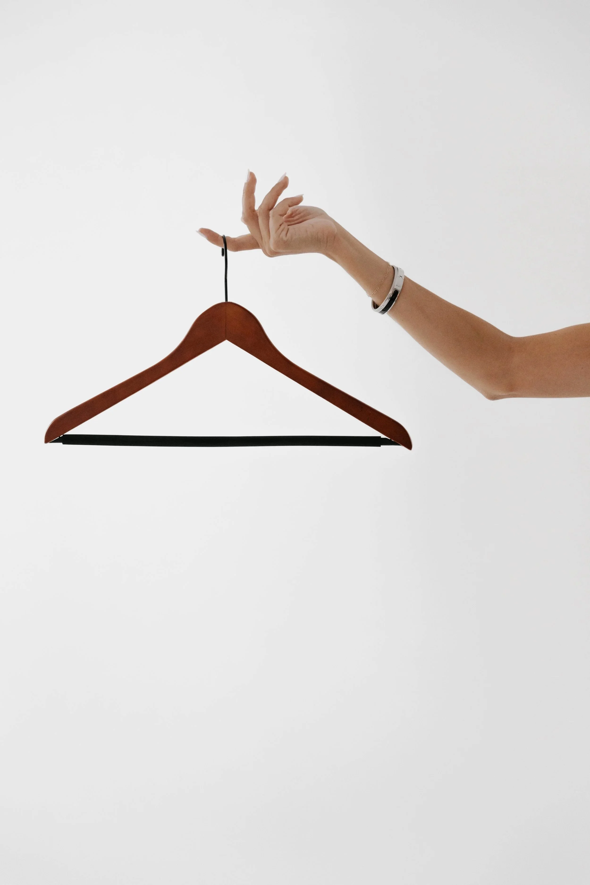Woman's hand holding a wood hanger in front of a white background. DistriktF Park City Pop Up Fashion Styling