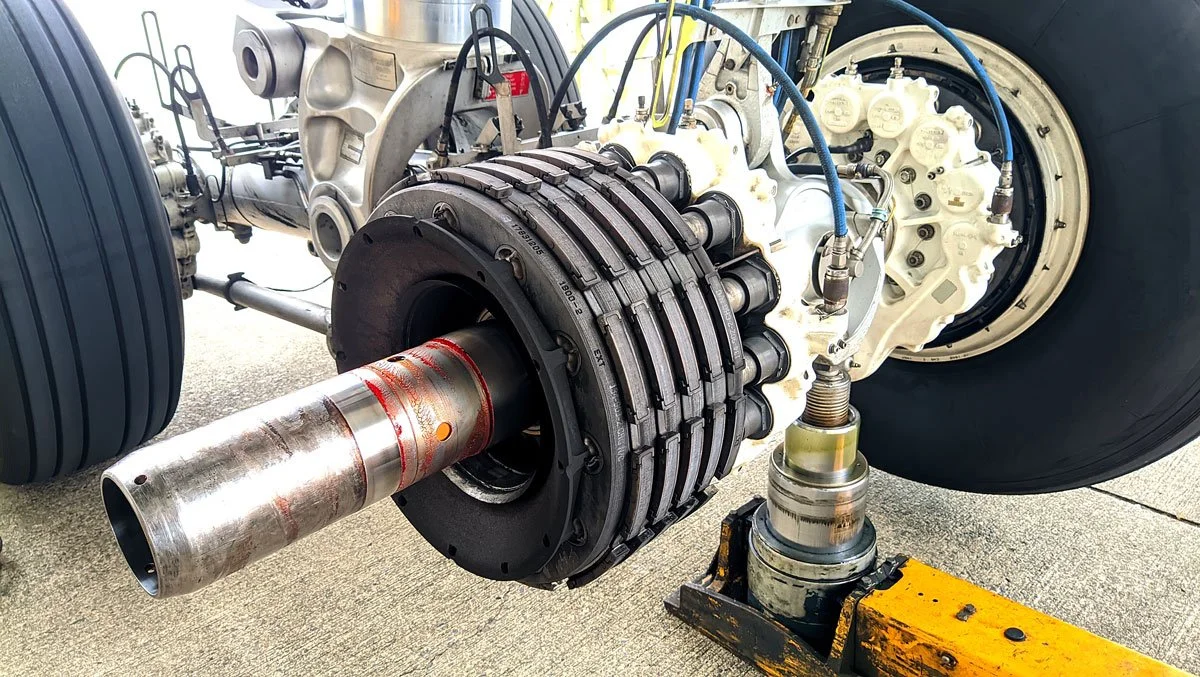 Mechanics working on airplane landing gear with steel axle