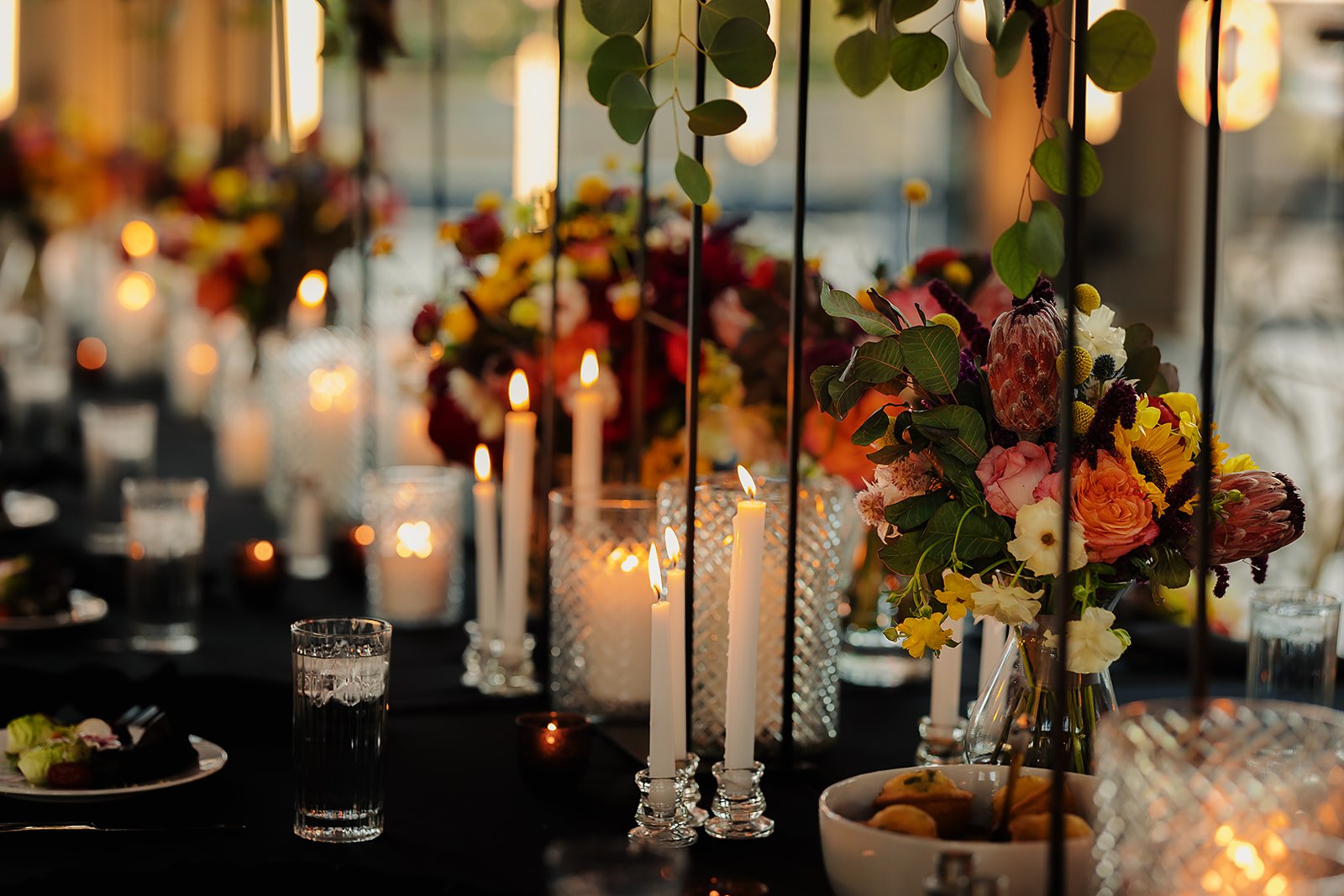 A long wedding reception table is decorated in deep autumn color tones and romantic taper candles.