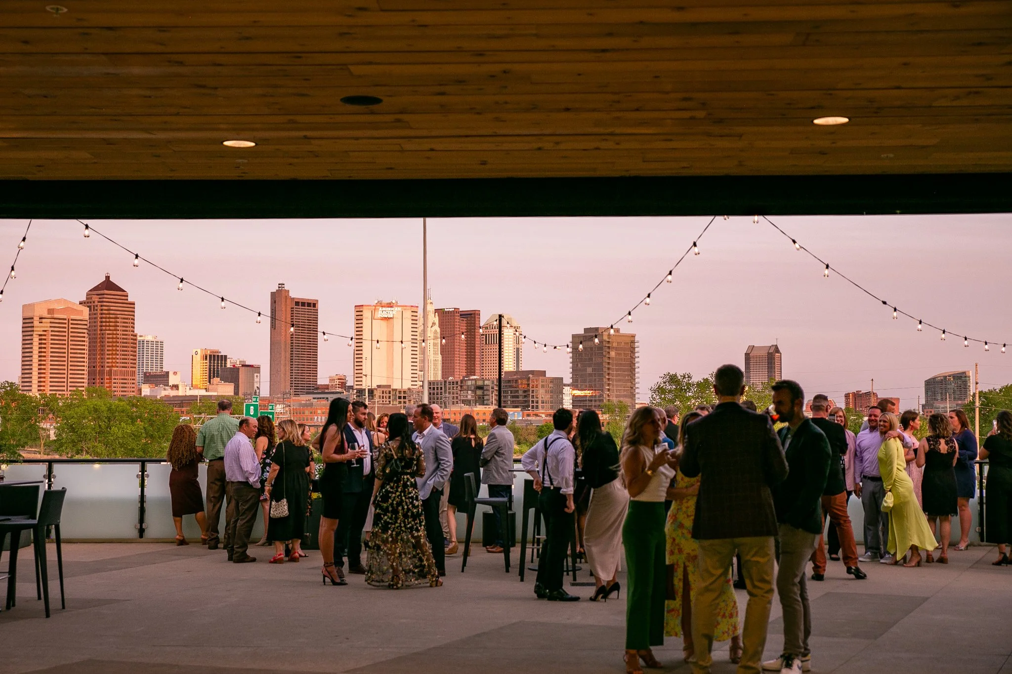 Professionals mingle under café lights during a weekday rooftop event at The Fives Columbus, combining skyline views with accessible, stylish event space.