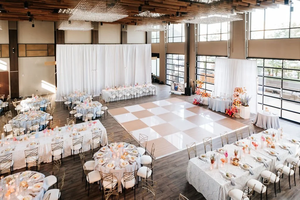 A spacious reception hall is decorated in soft color tones and pops of pink and peach, set and ready for a wedding reception.