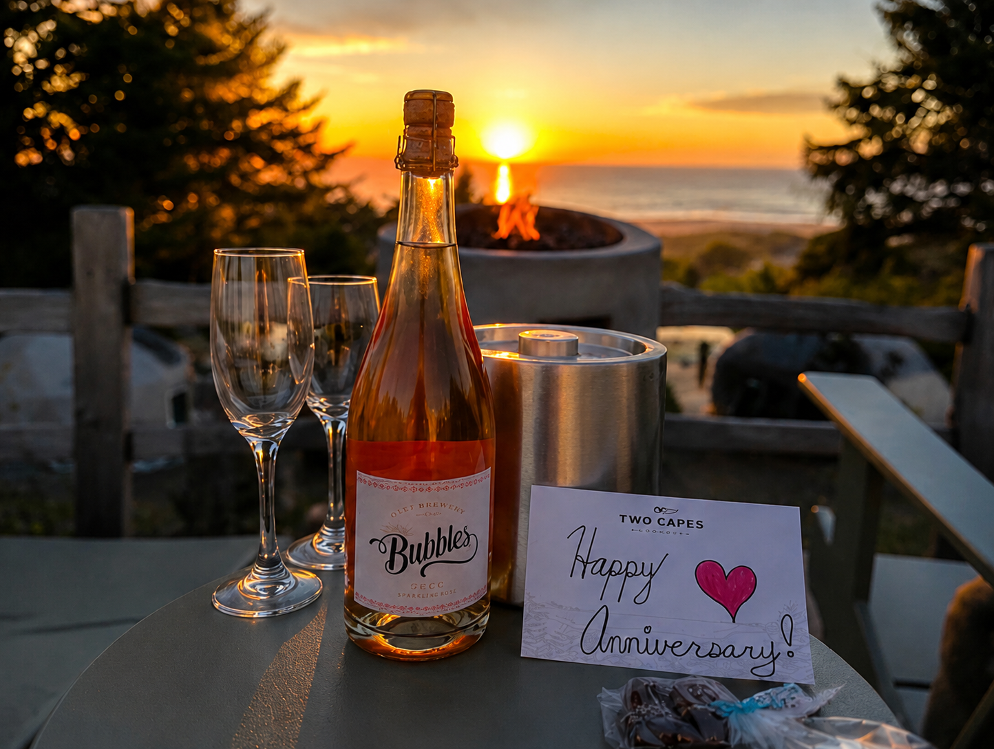 A bottle of wine with two glasses and chocolates before a beach sunset.