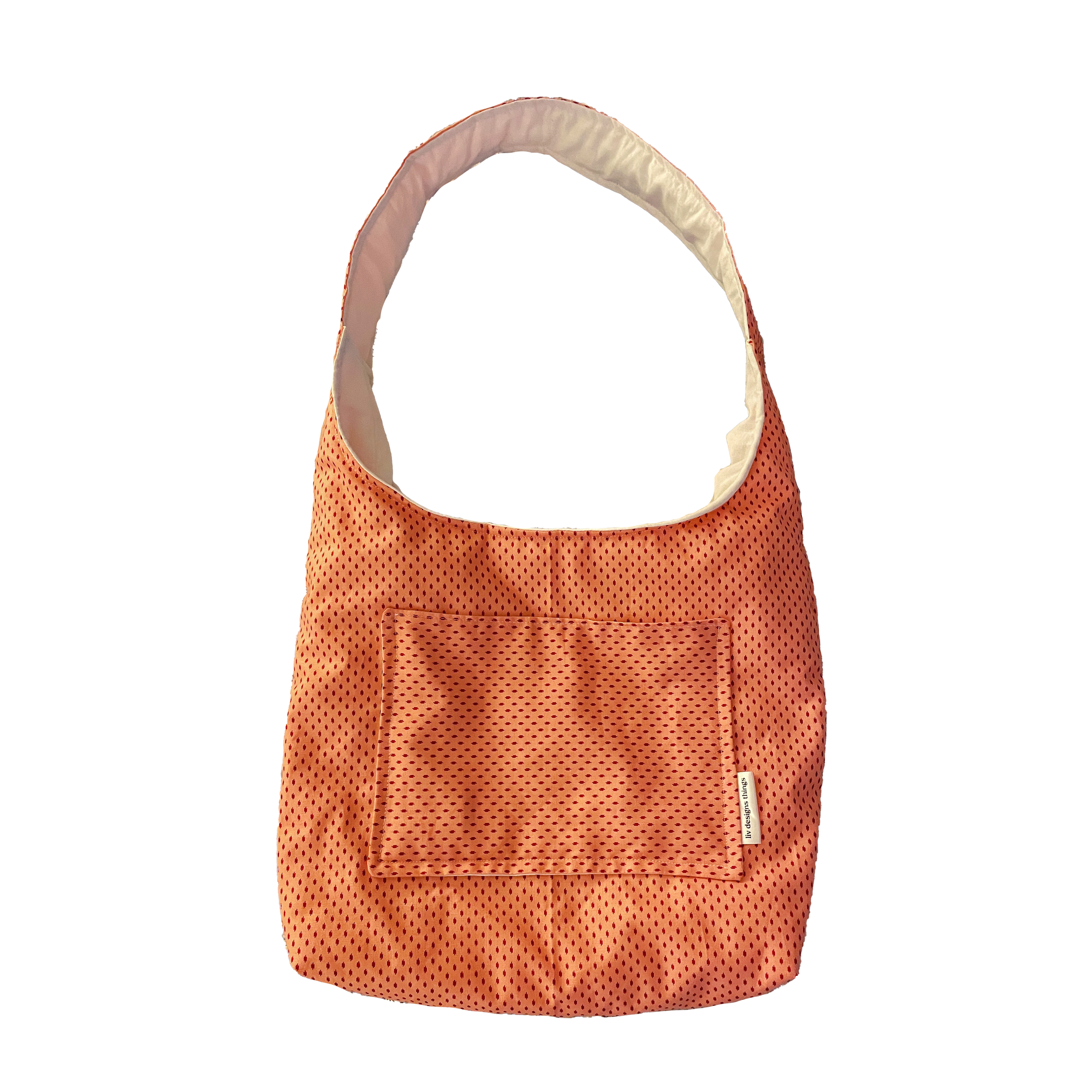 A pink and white pet carrier with a small pocket on the front, placed on a blue and white floral quilt.