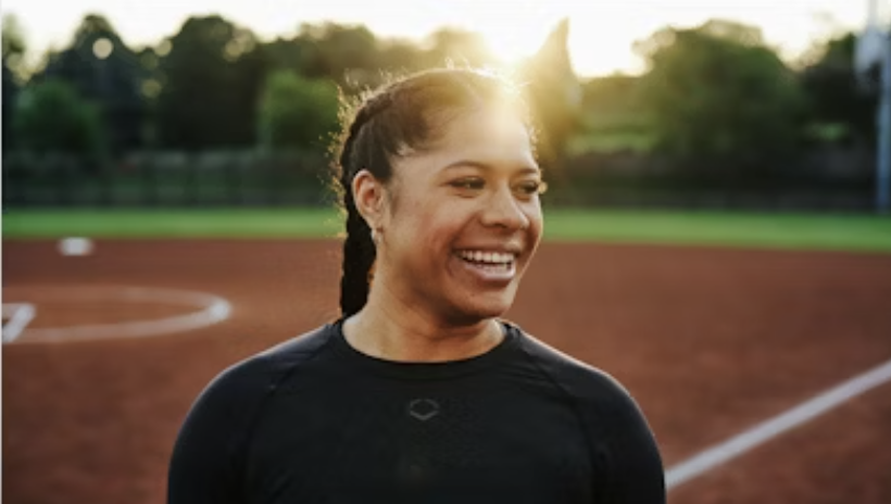 Smiling woman with braided hair on a sports field during sunset