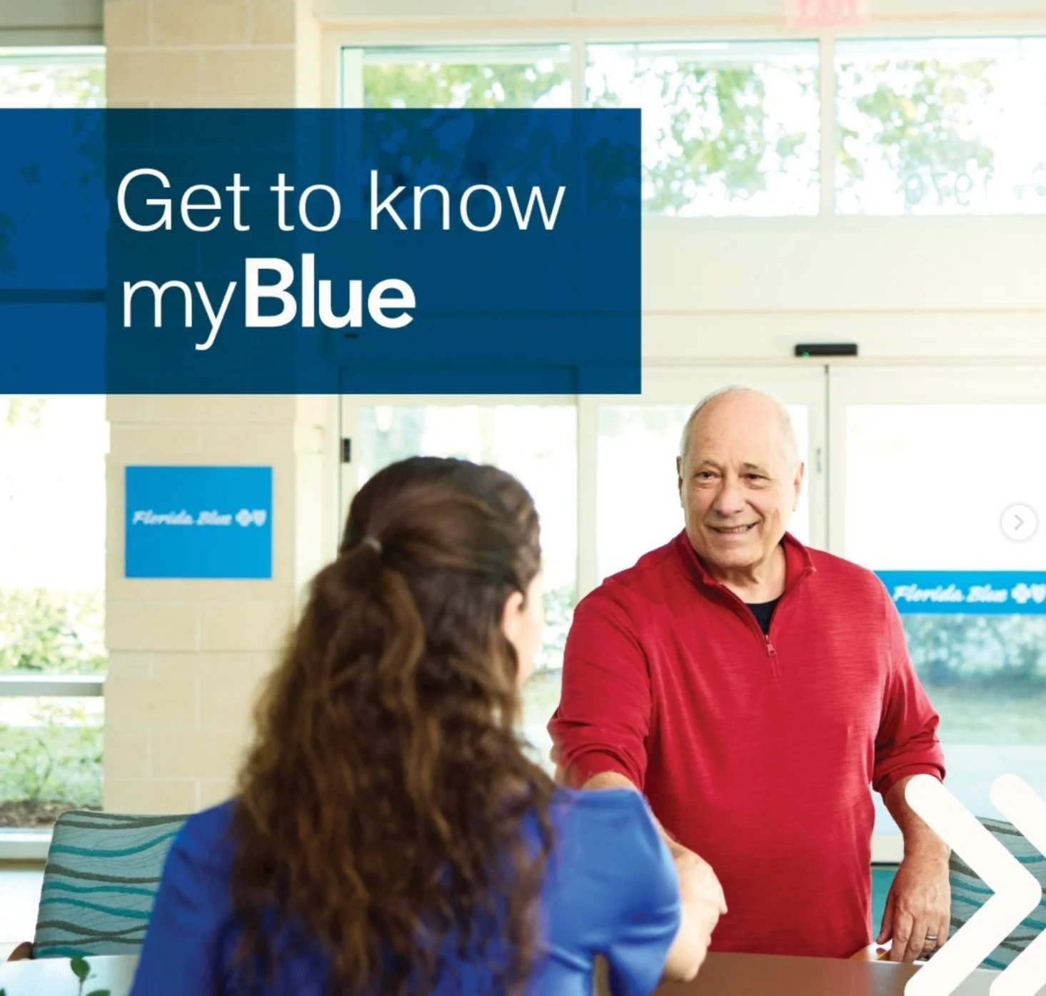 Two people talking inside a building with large windows, one man shaking hands with a woman. The setting advertises Florida Blue with banners and signs visible in the background.