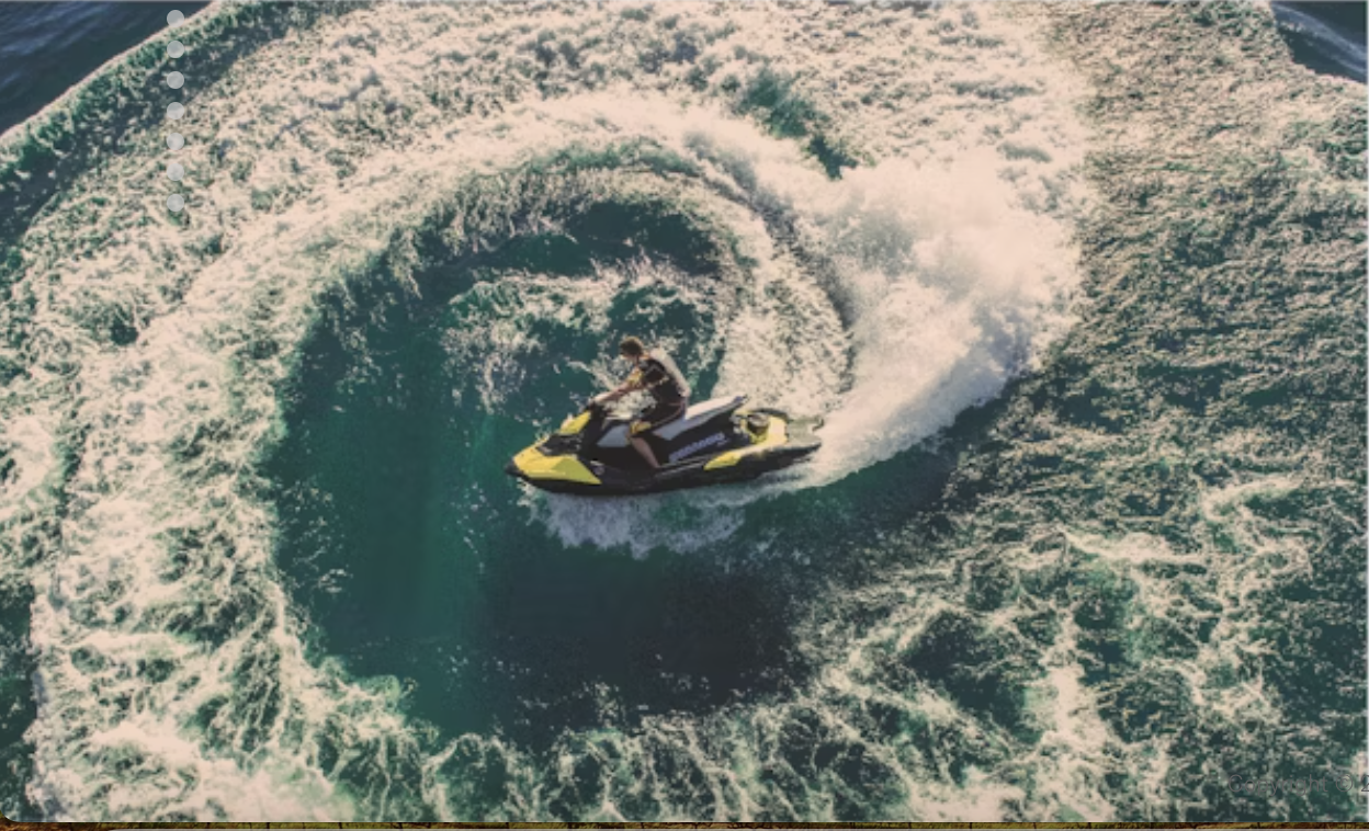Person riding a yellow and black jet ski on the ocean, creating a large splash.