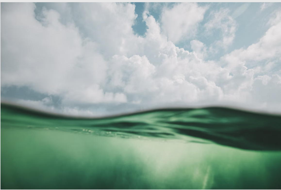 A view of the ocean with clear green water in the foreground and a partly cloudy sky above.