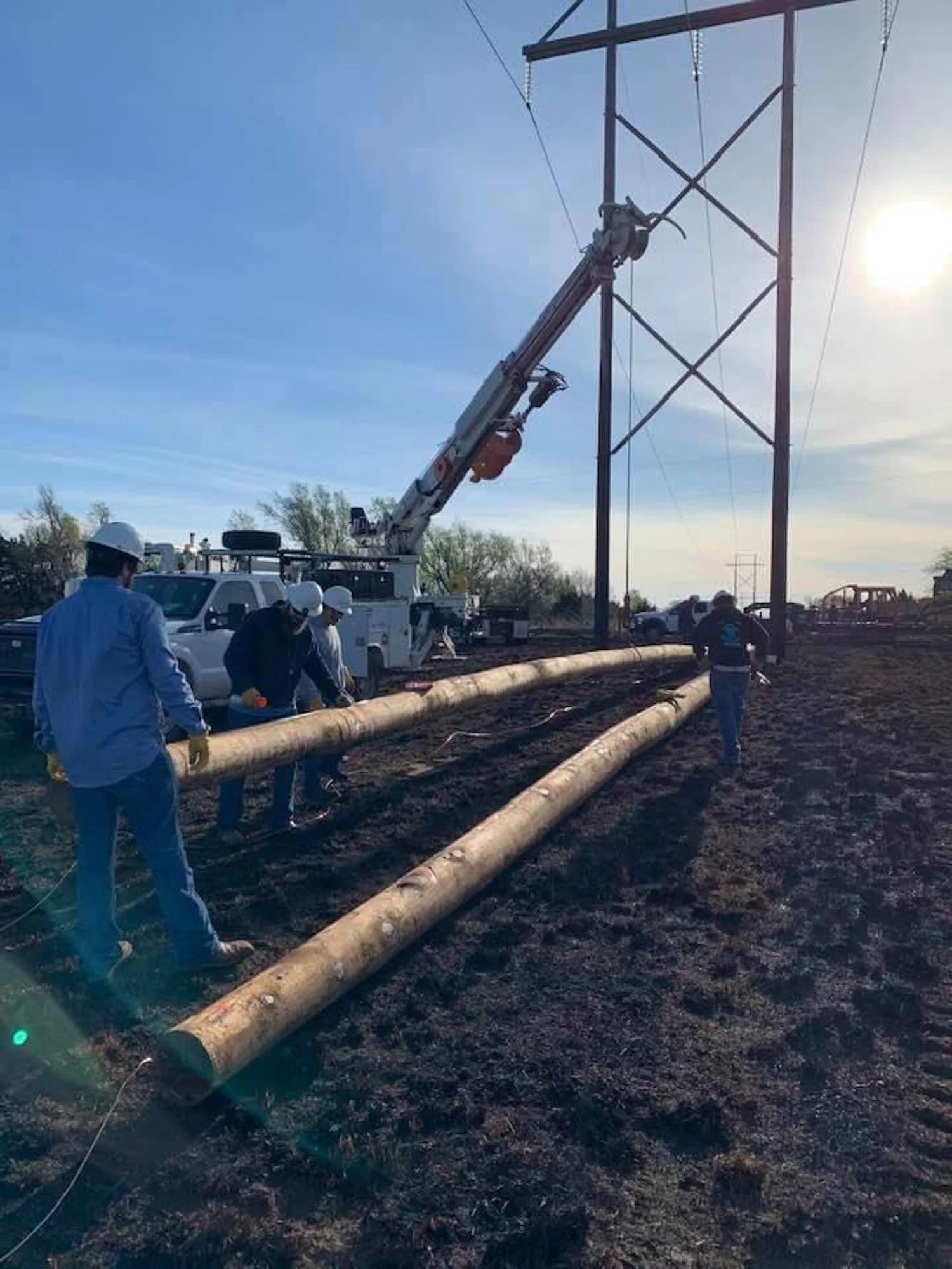 Workers installing power lines using wooden utility poles and a utility truck with a crane.