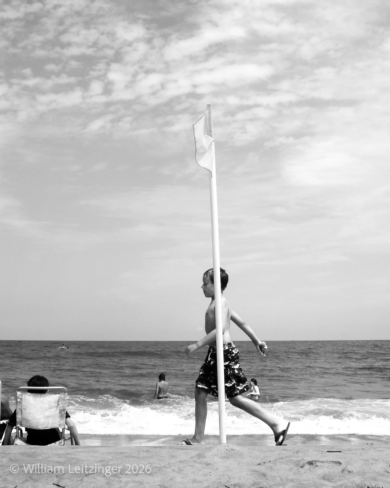 20090813-Vacation-Travel-Beach-MD-Ocean_City-Boy_Walking_Past_Flag_on_Beach-01-B&W-Cropped_8x10-(Copyright).jpg