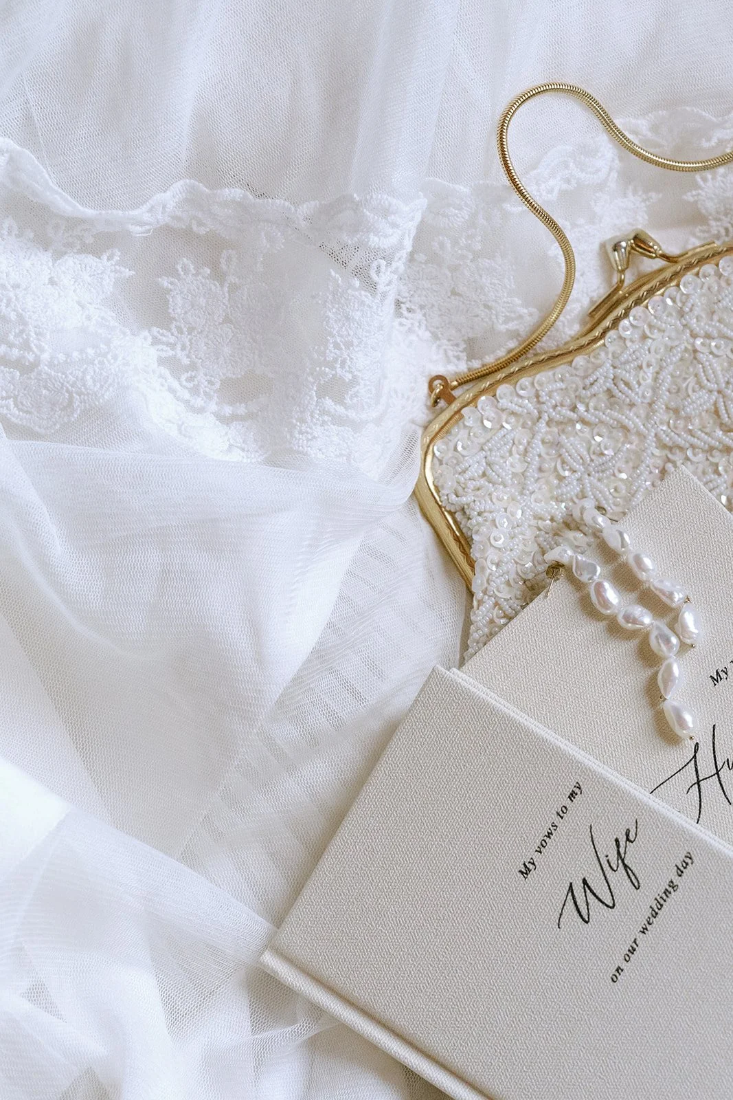 Wedding details laid against a wedding gown, a reception gown, and a lace-trimmed wedding veil.