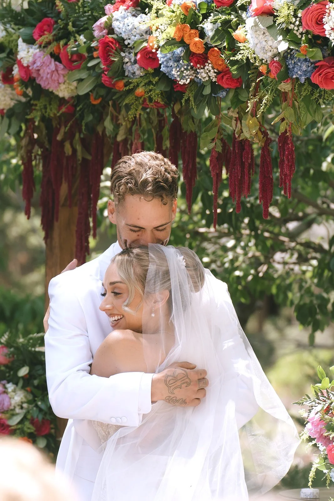 The bride and groom hug after the outdoor wedding ceremony under a colorful floral arbor in Big Bear California