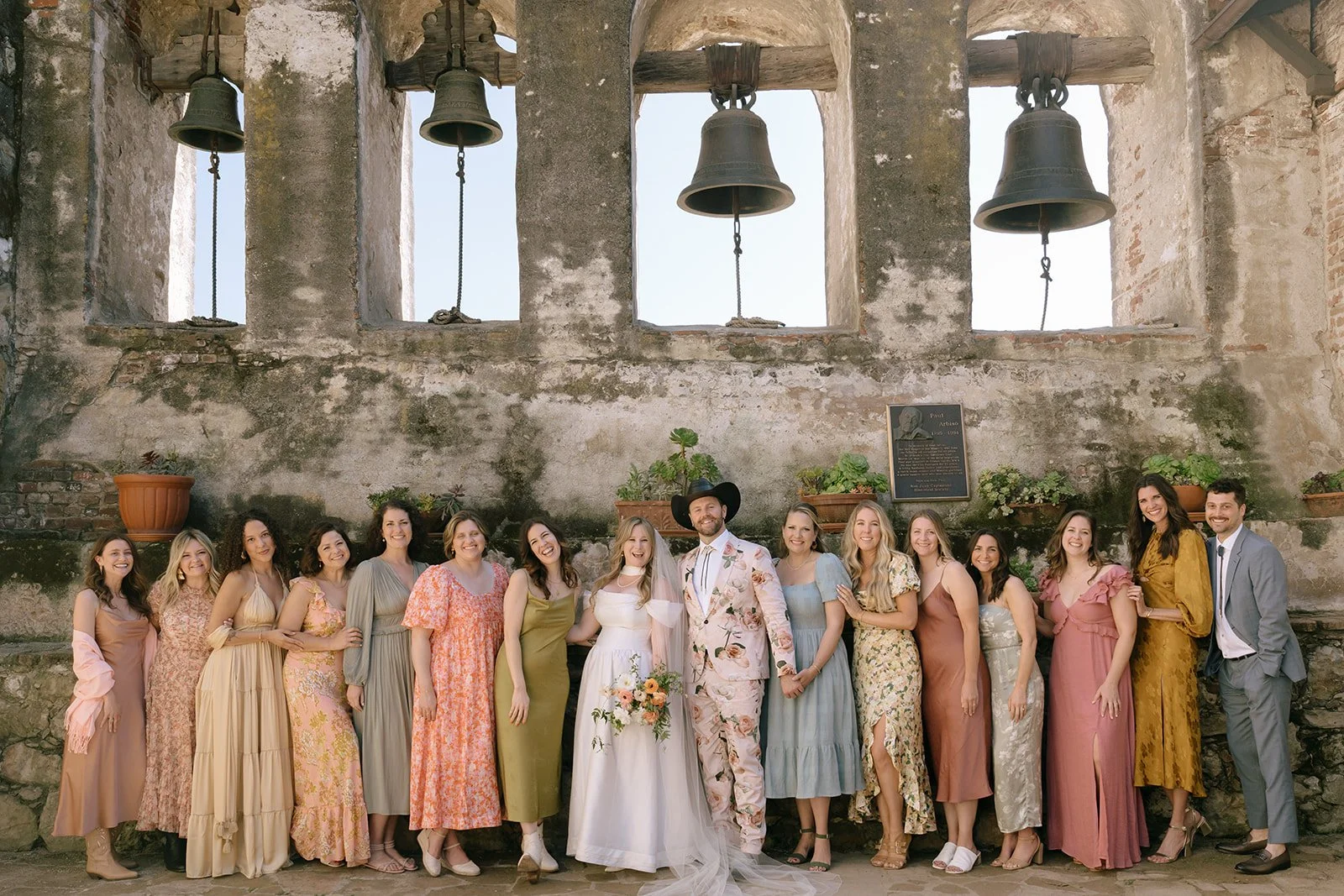 The bridal party wears garden-inspired gowns and smiles for portraits at the mission.