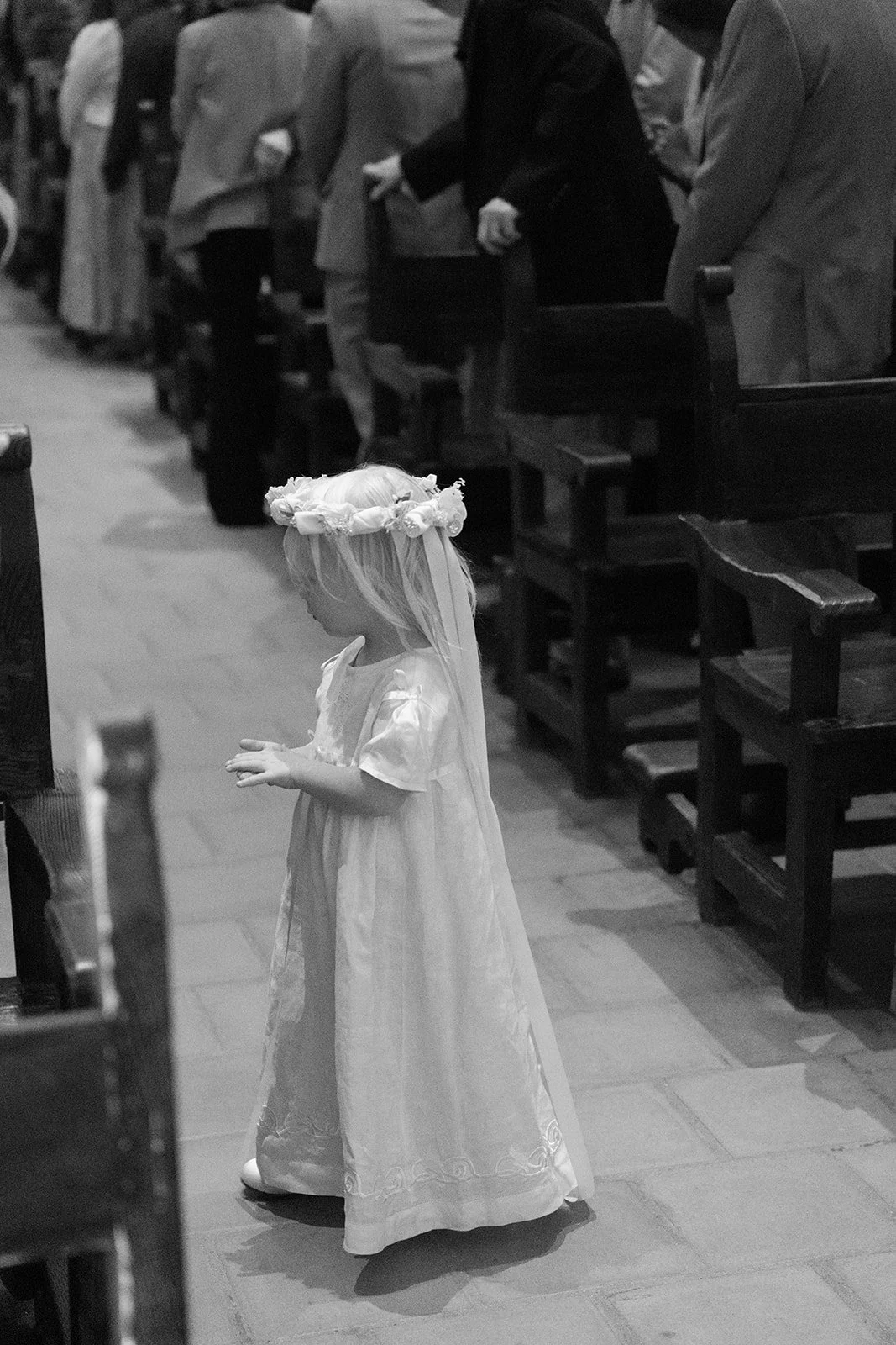 The flower girl wears a crown of flowers and ribbons and finds her seat.