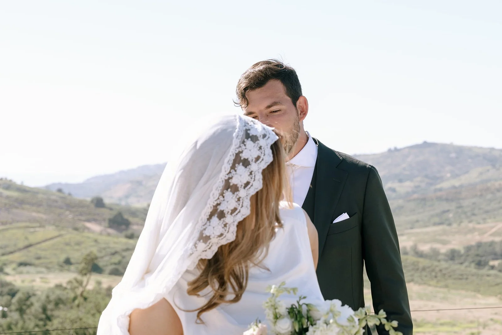 Groom admires bride's hand-made, lace-trimmed, tiered mantilla veil.