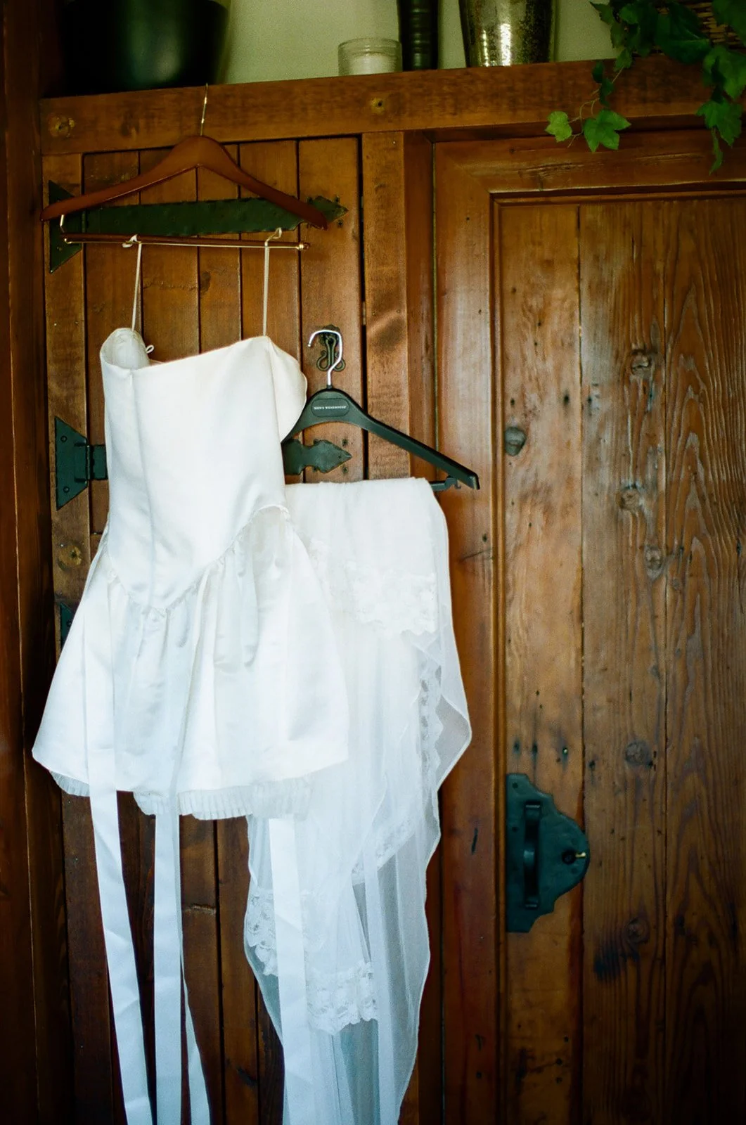 Bridal reception mini dress hangs with custom tiered lace-trimmed mantilla veil. Analog 35 mm film.