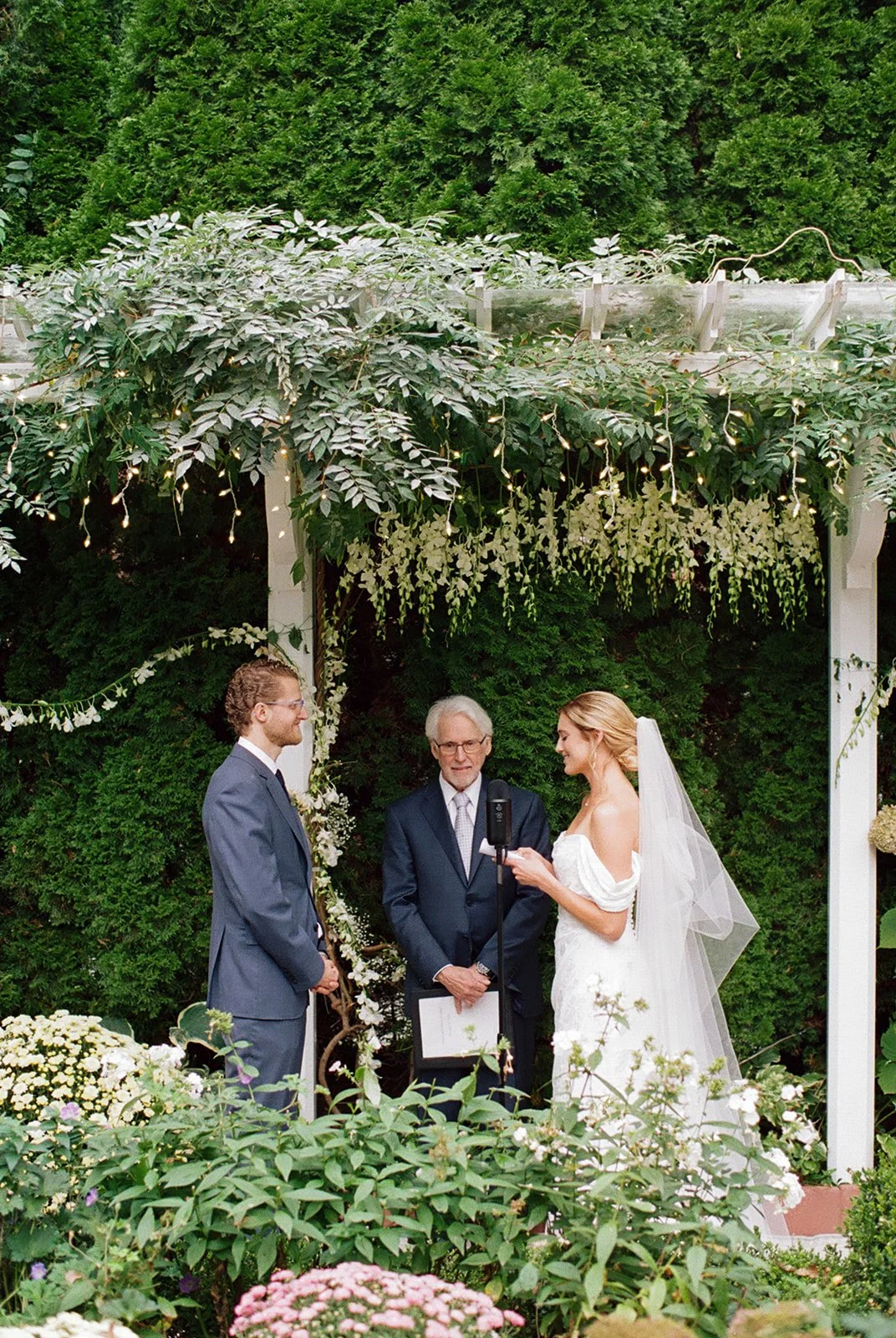 Bride and groom stand under floral trellis to exchange vows. Color 35 mm film
