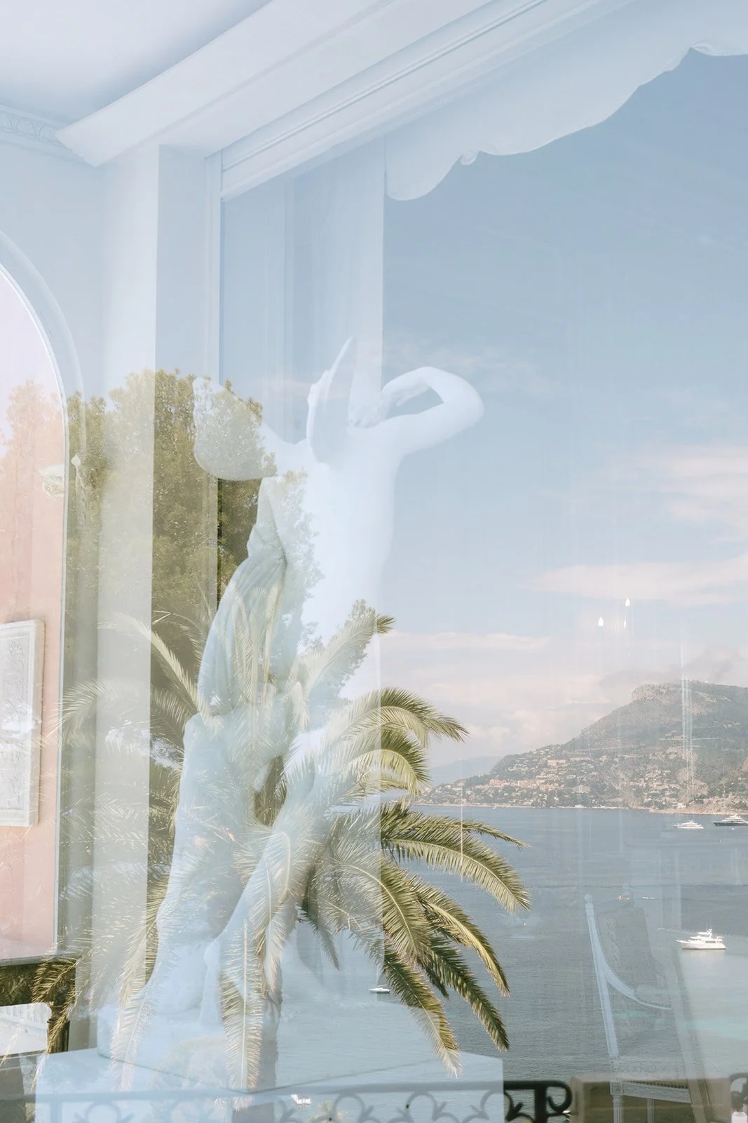 A marble statue inside the Villa Ephrussi through a window reflecting the Mediterranean Sea and Villefranche-sur-Mer