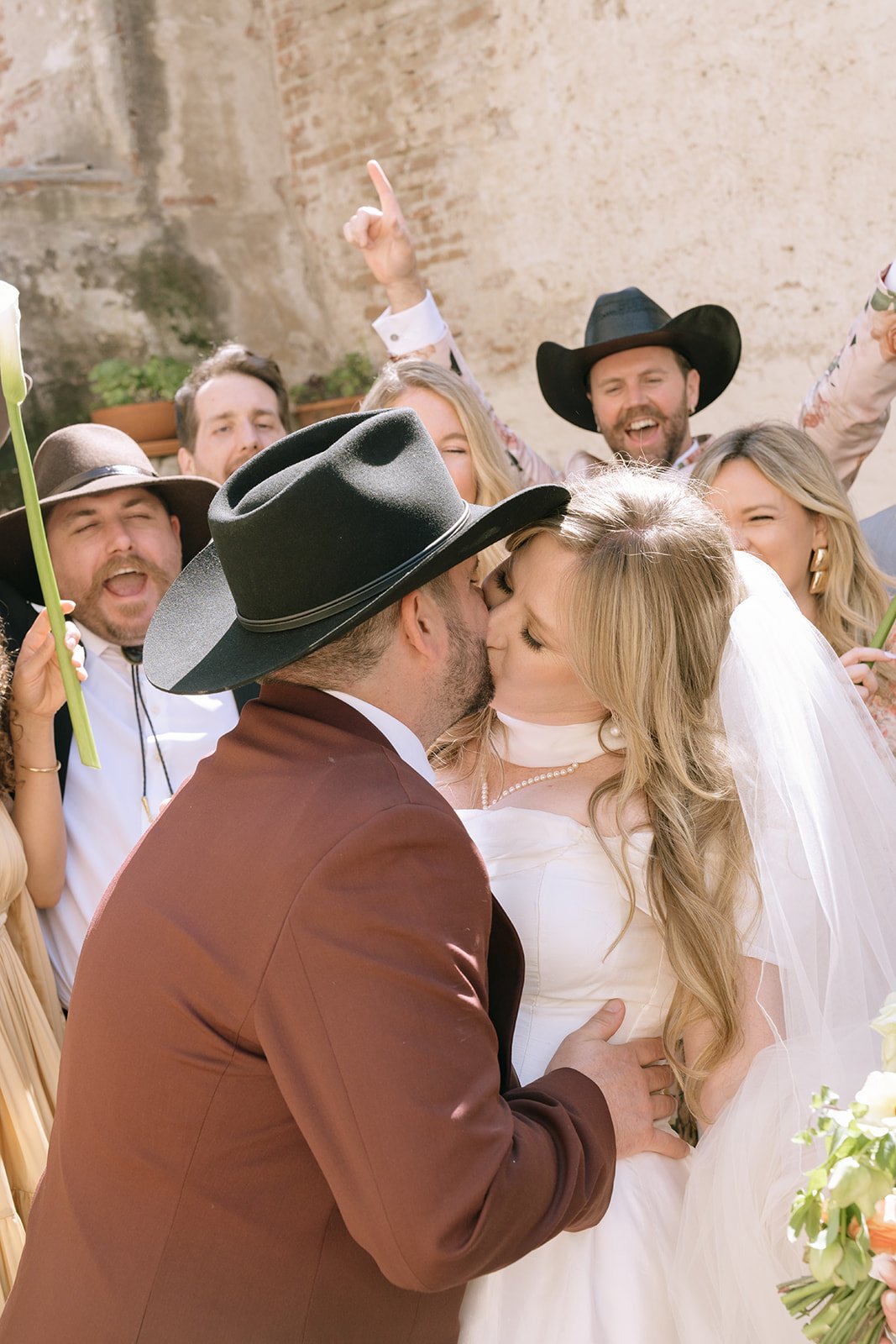 Wedding party portraits where everyone cheers and the couple kisses