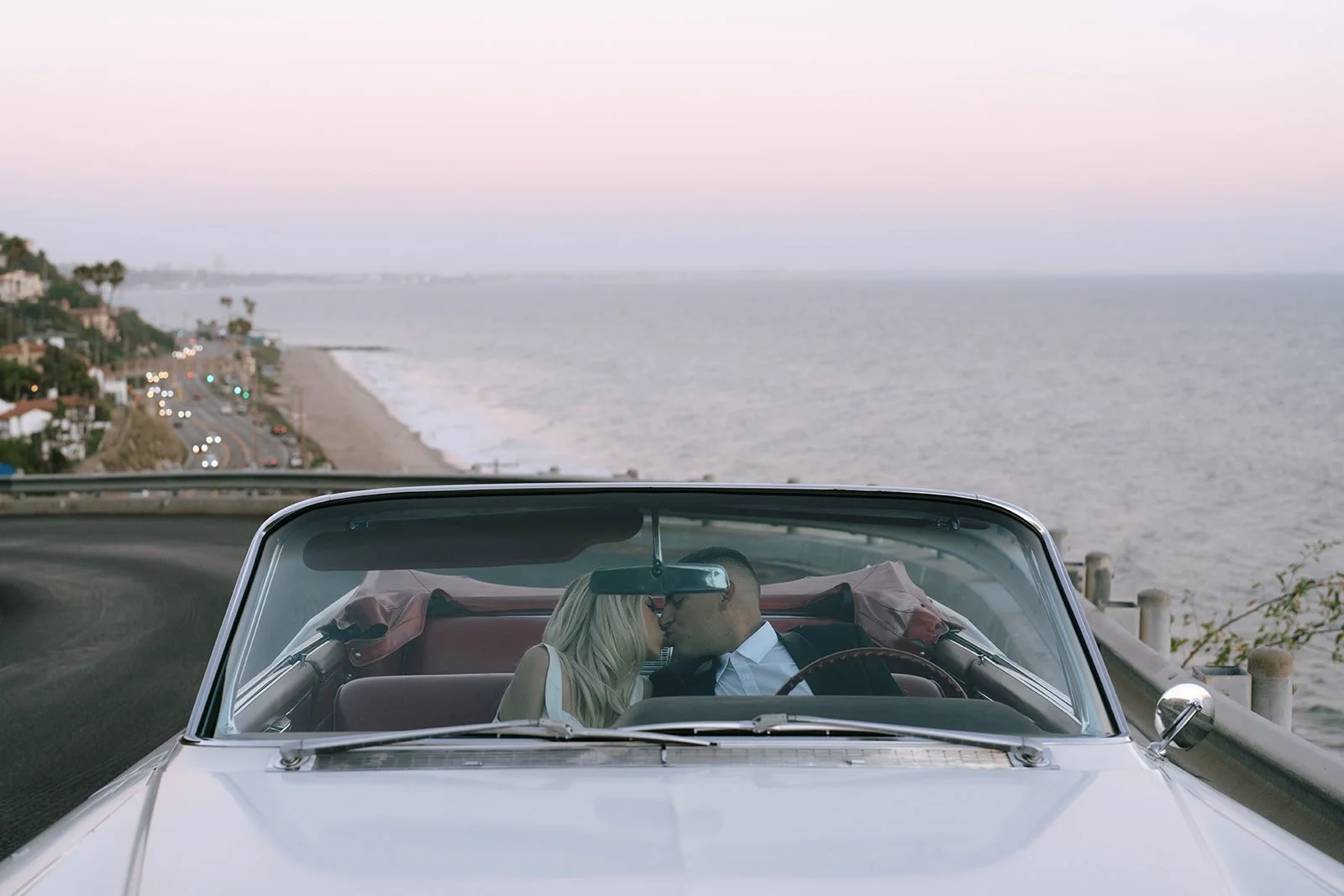 The couple kissing in the car with the beach behind them