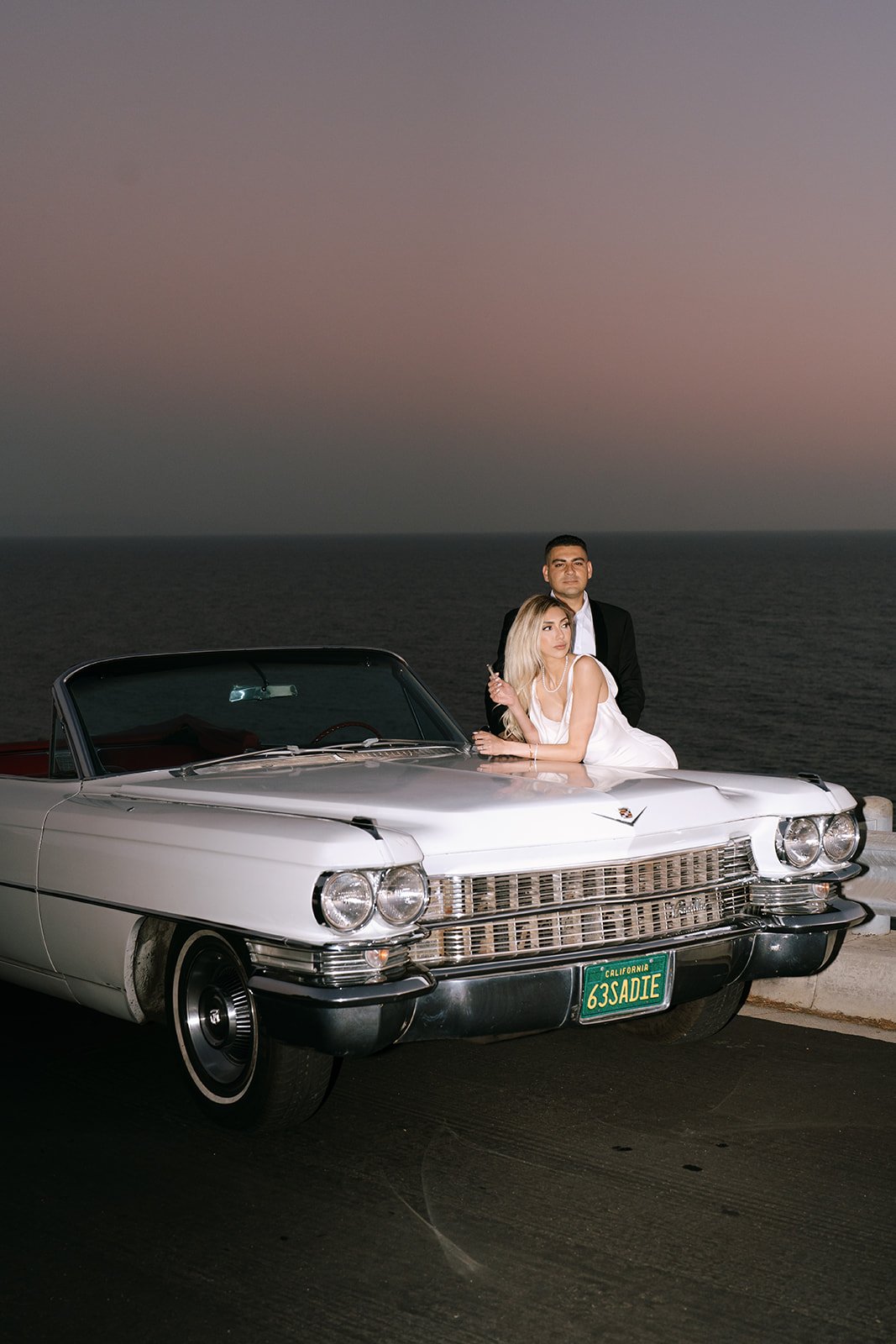 The couple posing with the car and the beach behind them