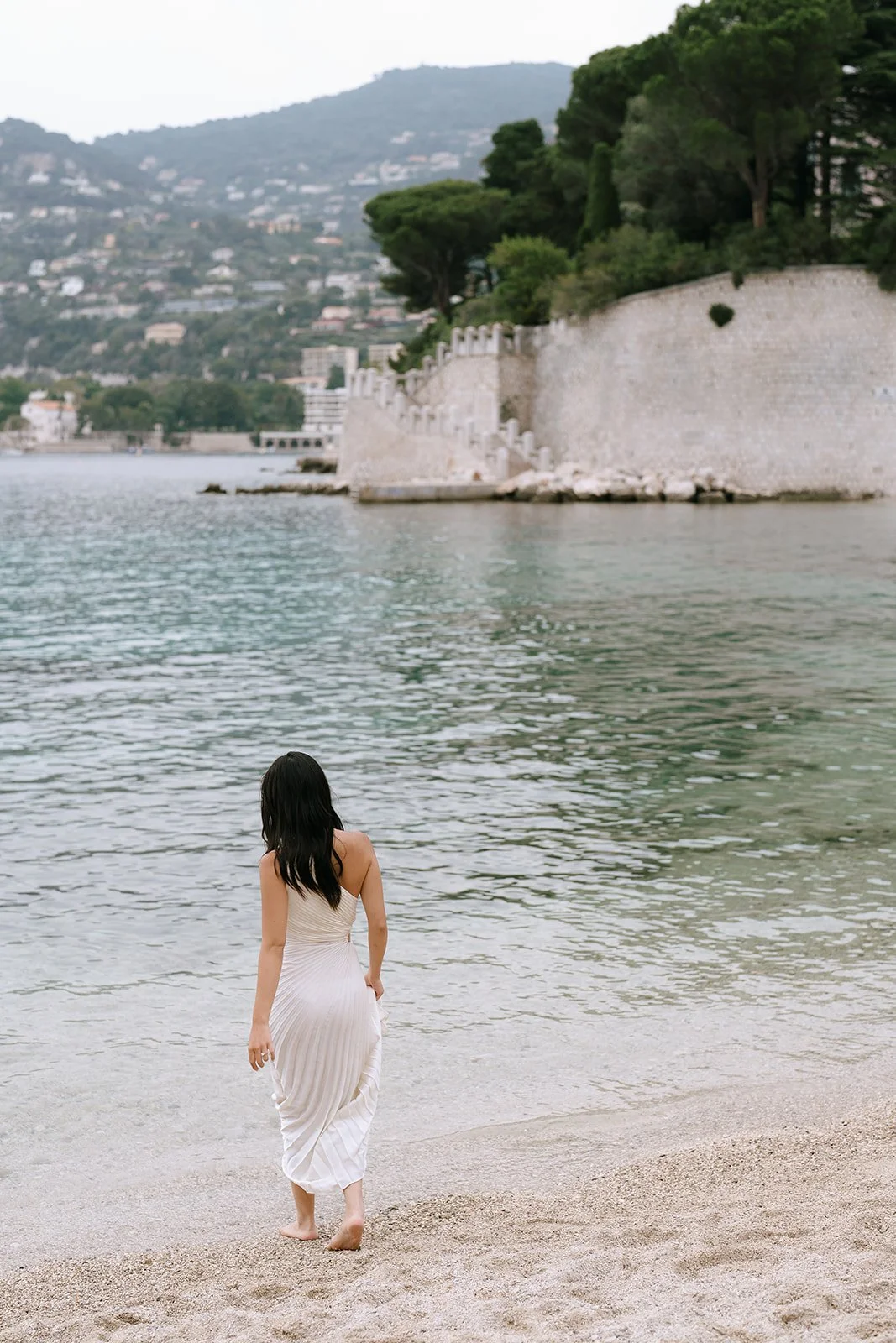 Bride to be walks into the Mediterranean Sea on the French Riviera in a white one-sleeve dress