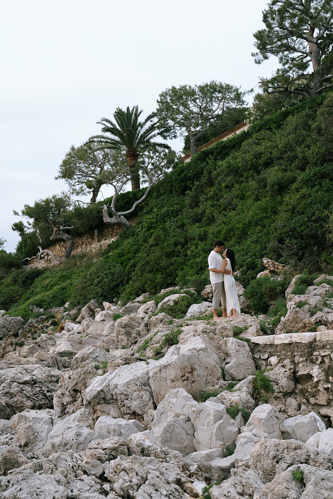Couple standing together surrounded by coastal limestone rocks and greenery on the edge of the French Riviera on the Saint-Jean-Cap-Ferrat coastline