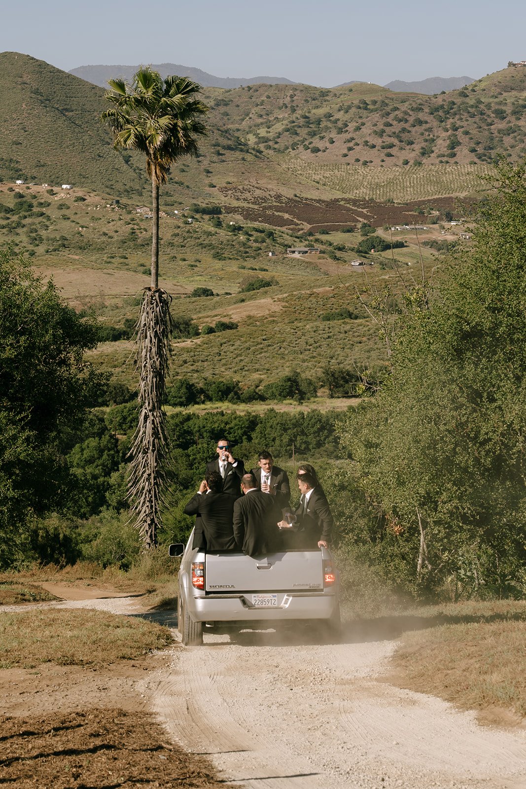 Groomsmen ride the back of a truck to the reception.