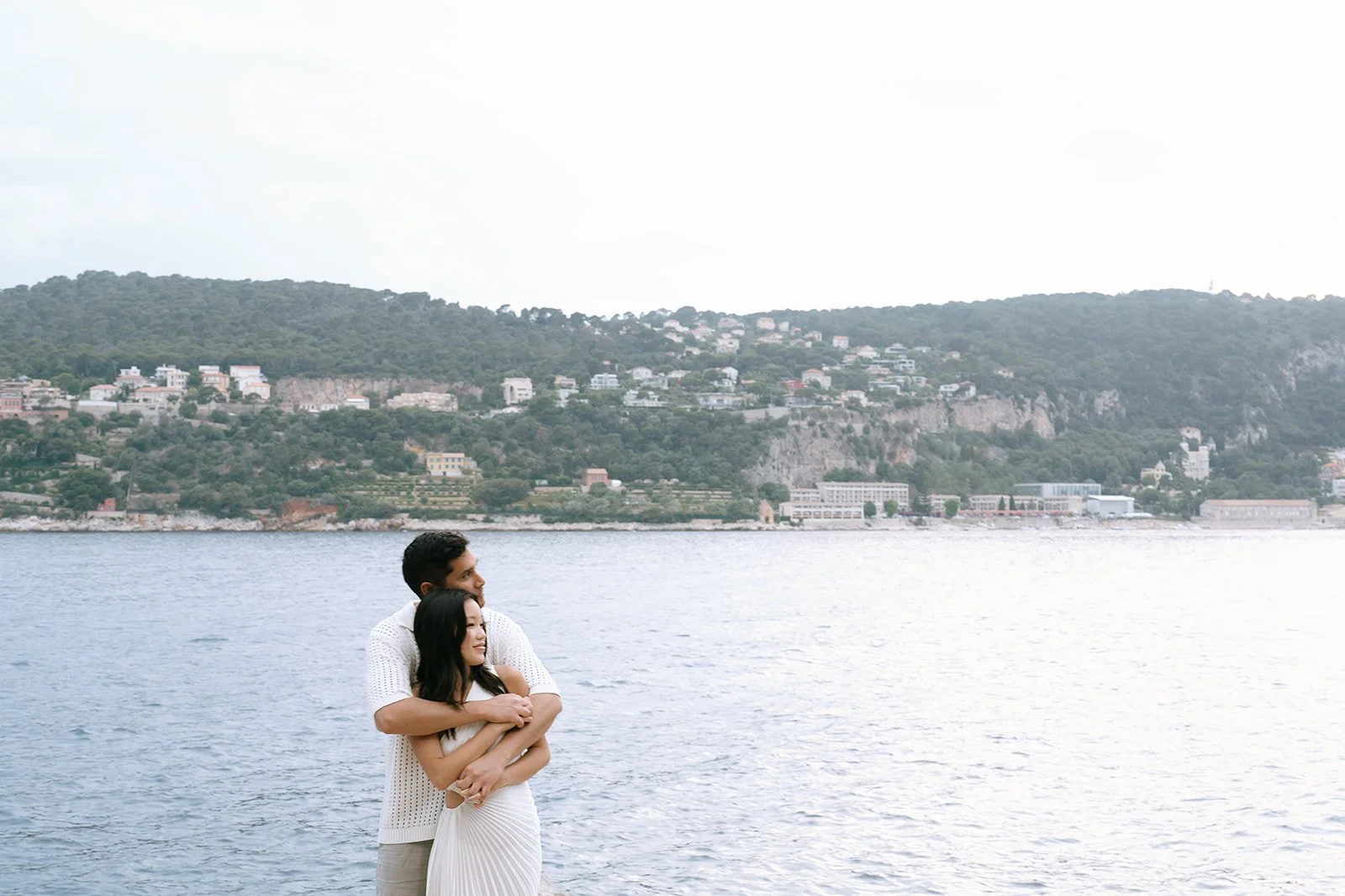Couple looking across the Bay of Villefranche to the Villefranche Sur Mer resort town on the French Riviera during their destination engagement photoshoot