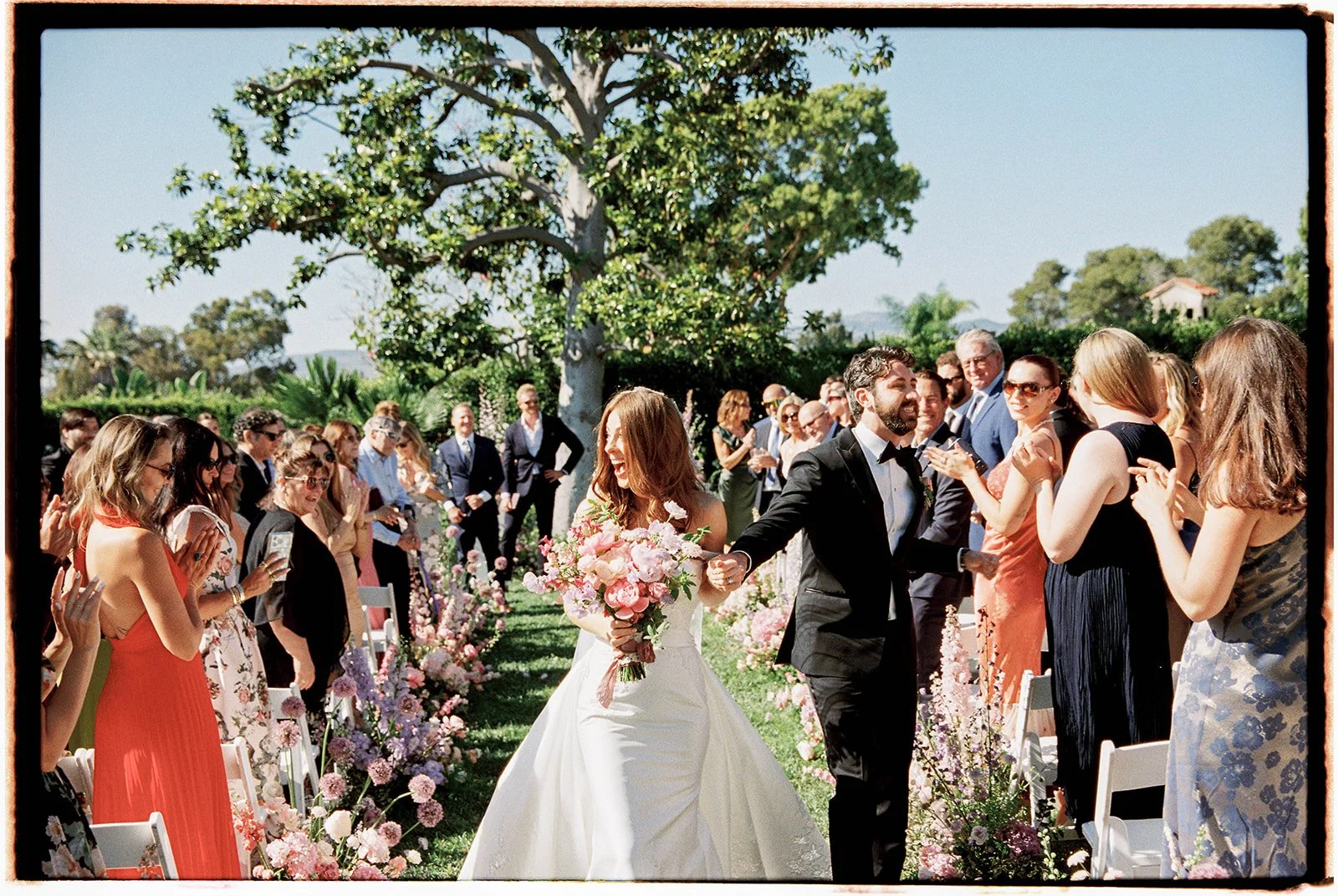  The newlyweds greeting loves ones in the flower filled aisle. 35 mm film. 