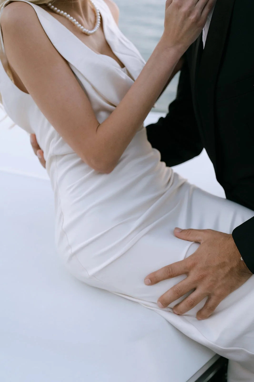 Close-up of a pearl necklace and the groom's hand.