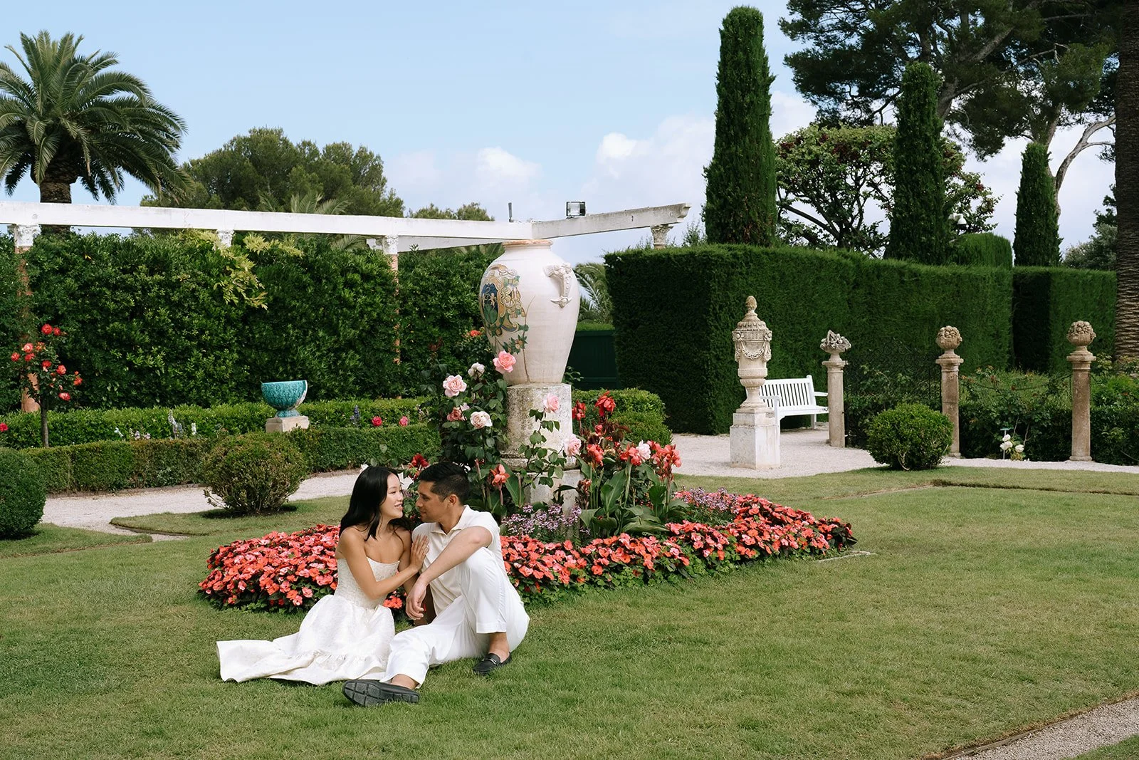 Soon to be bride and groom sit together on the green grass in the French garden of the Villa Ephrussi during their destination engagement session on the South of France