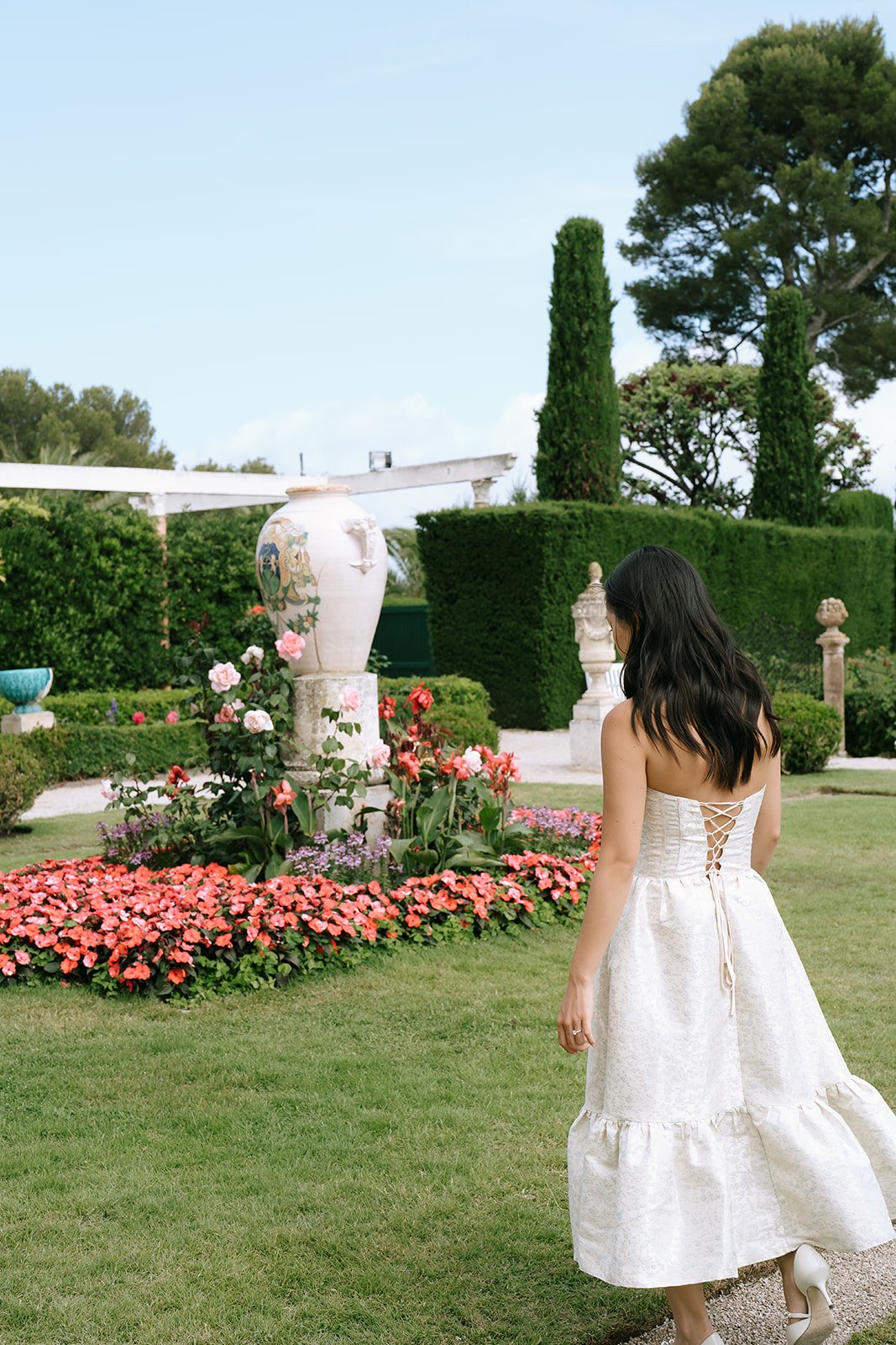 Bride in a lace-up corset style white dress walking into the French garden of the Villa Ephrussi