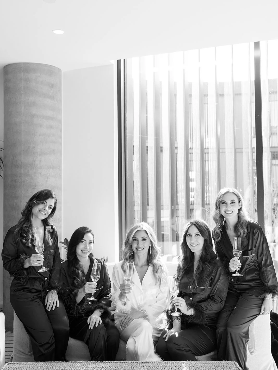 The bride and bridesmaids sitting on a couch drinking champagne.