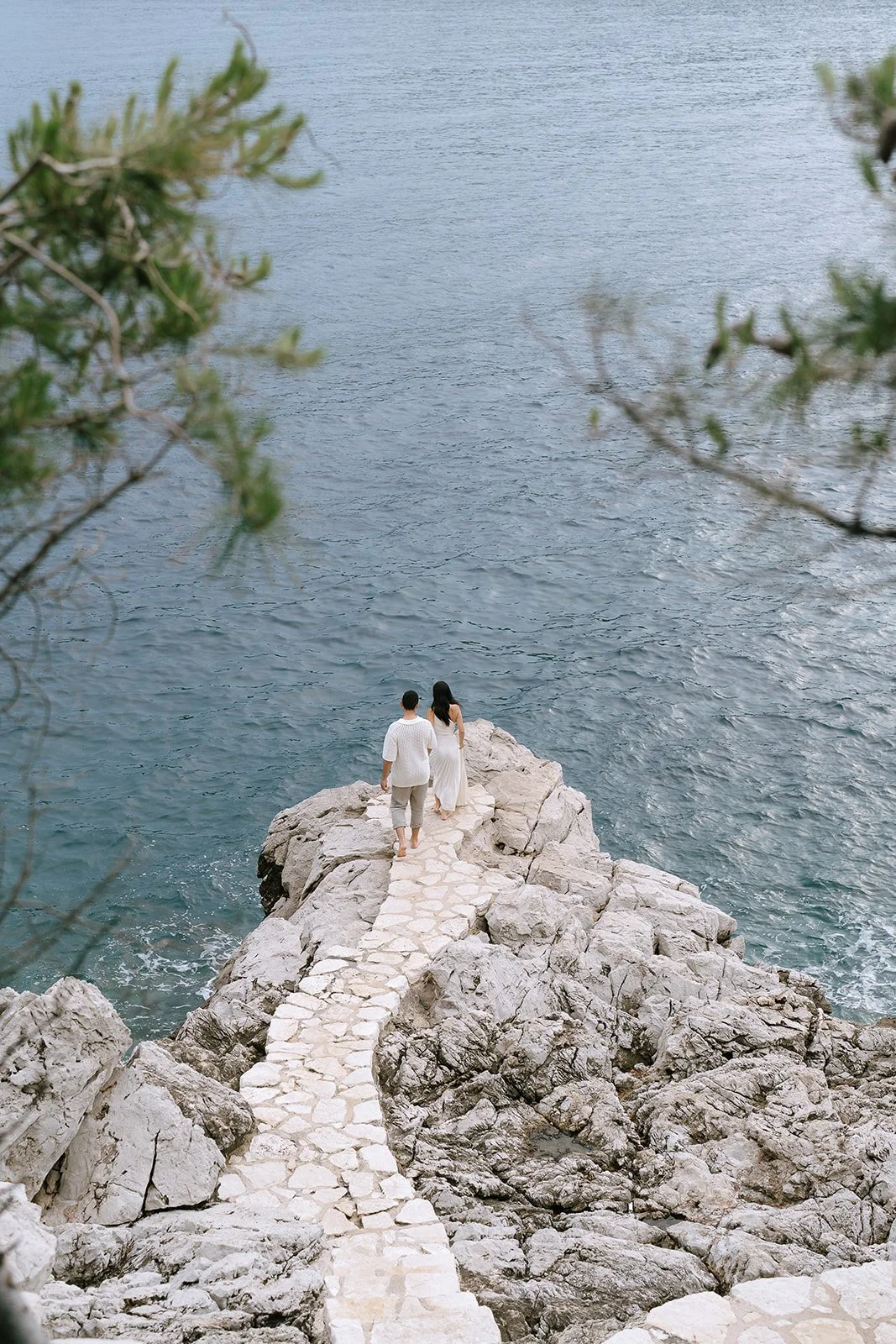 Couple walking along a cobblestone path leading to a lookout of the Rade de Villefranche sur Mer during their destination engagement photoshoot on the South of France