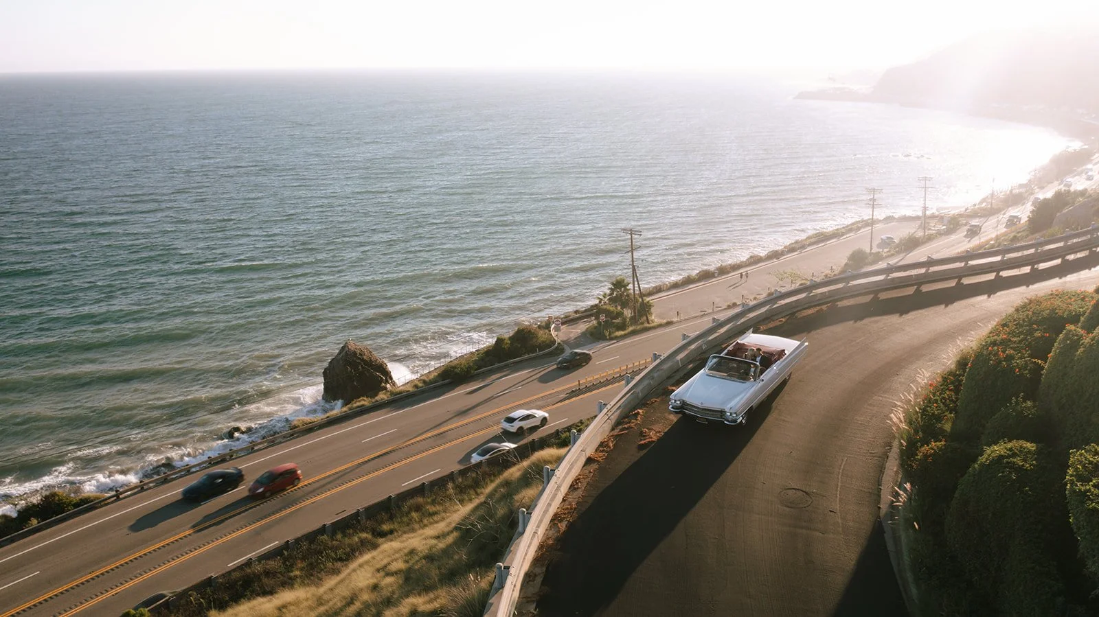digital drone photo of a white luxury vintage convertible car driving down the malibu coast of california