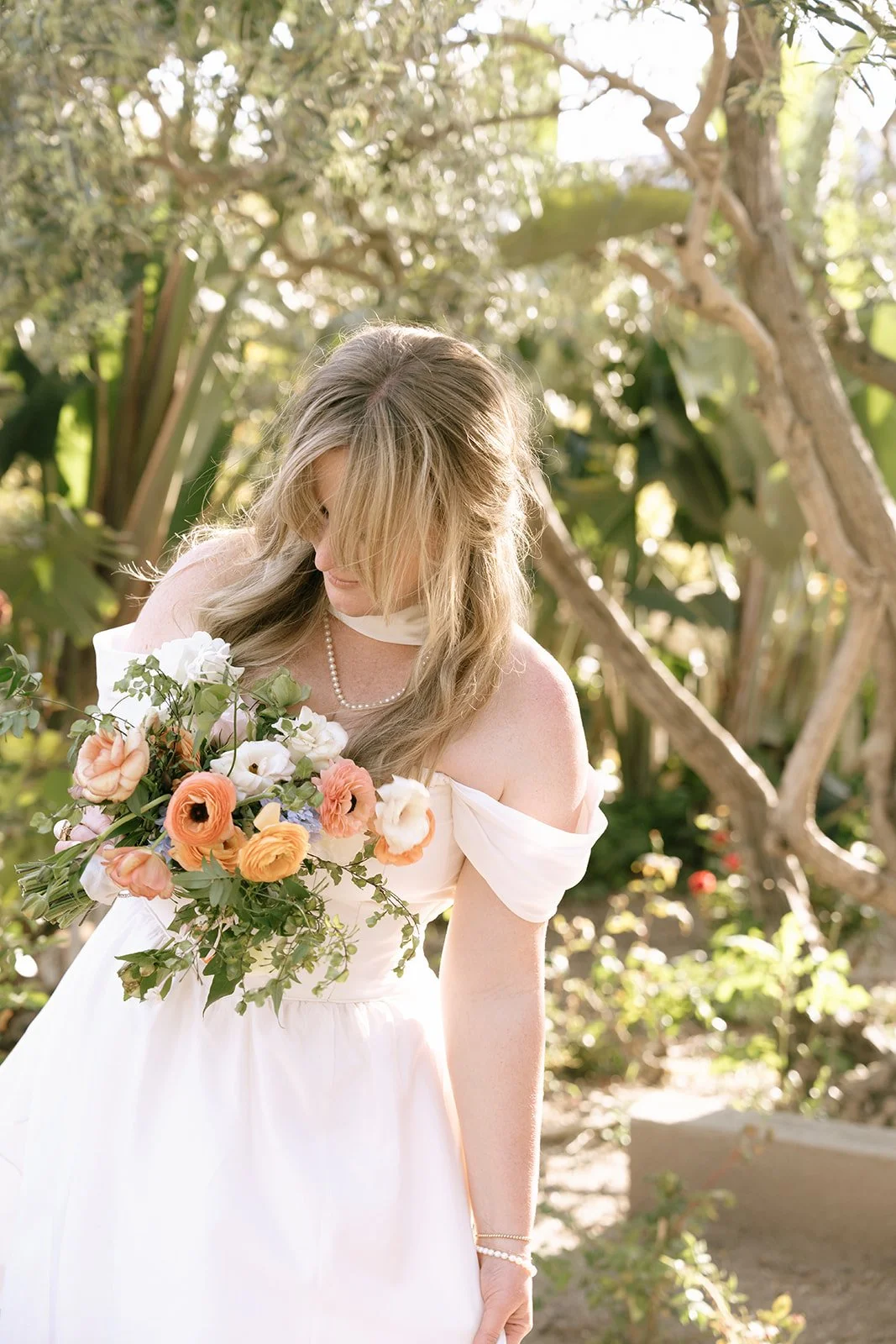The bride wears pearls around her wrist and  neck, a vintage gown, a bridal scarf,  and a garden-inspired bouquet full of bright and cheerful colors
