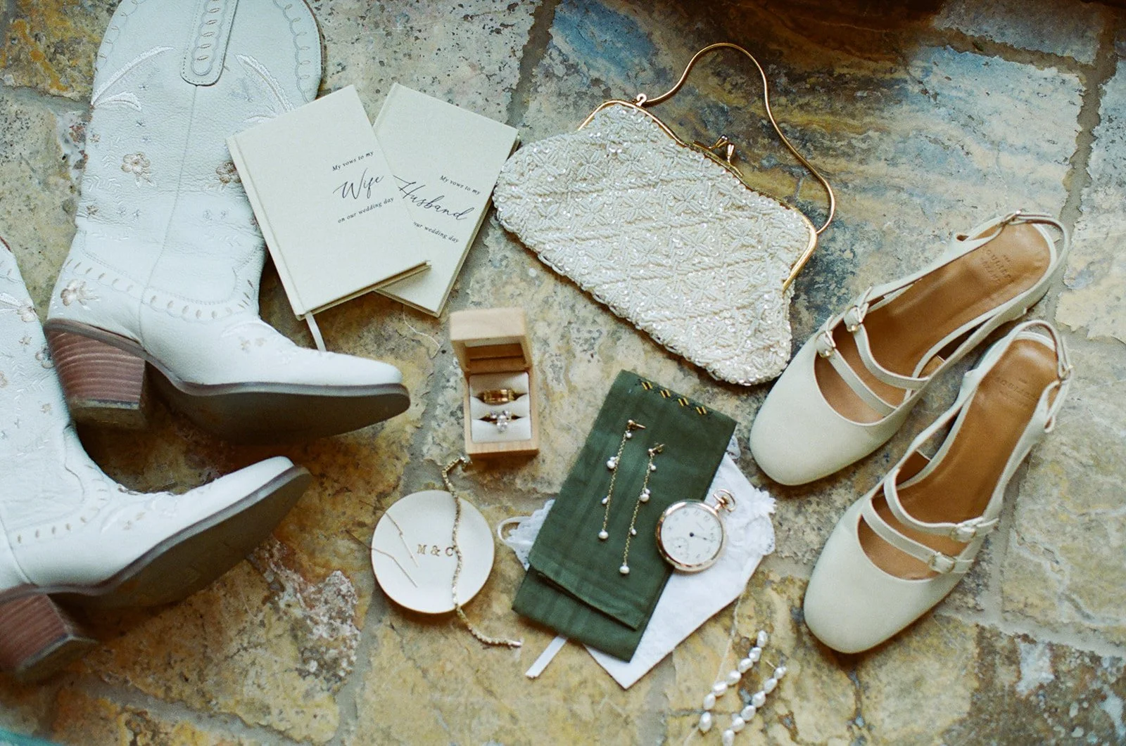 Wedding details: linen vow books, a vintage purse, pearl drop earrings, wedding rings, a signature ring dish, vintage-inspired heels, and custom white cowgirl boots. Analog 35 mm film.