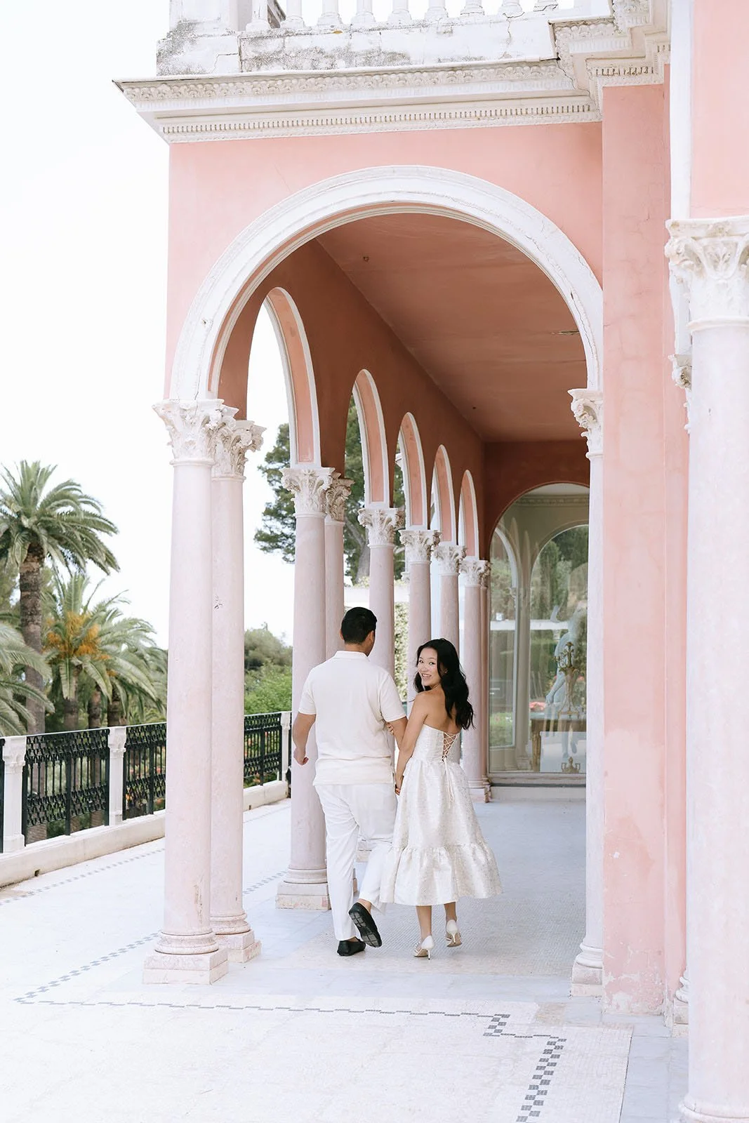 Soon to be bride and groom walk under an arched colonnade of the Villa Ephrussi during their destination engagement session