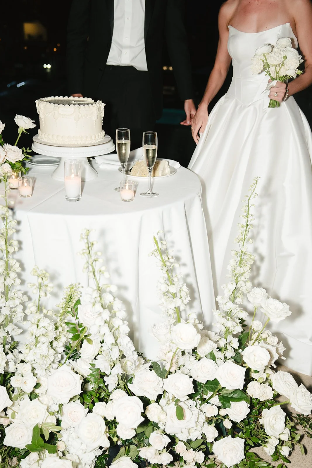 A wedding cake with a white roses and delphinium surrounding