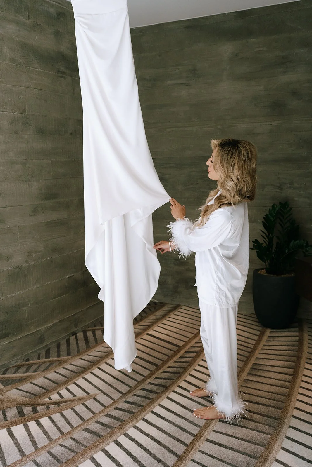 bride in fluffy pajamas admires minimalist wedding gown