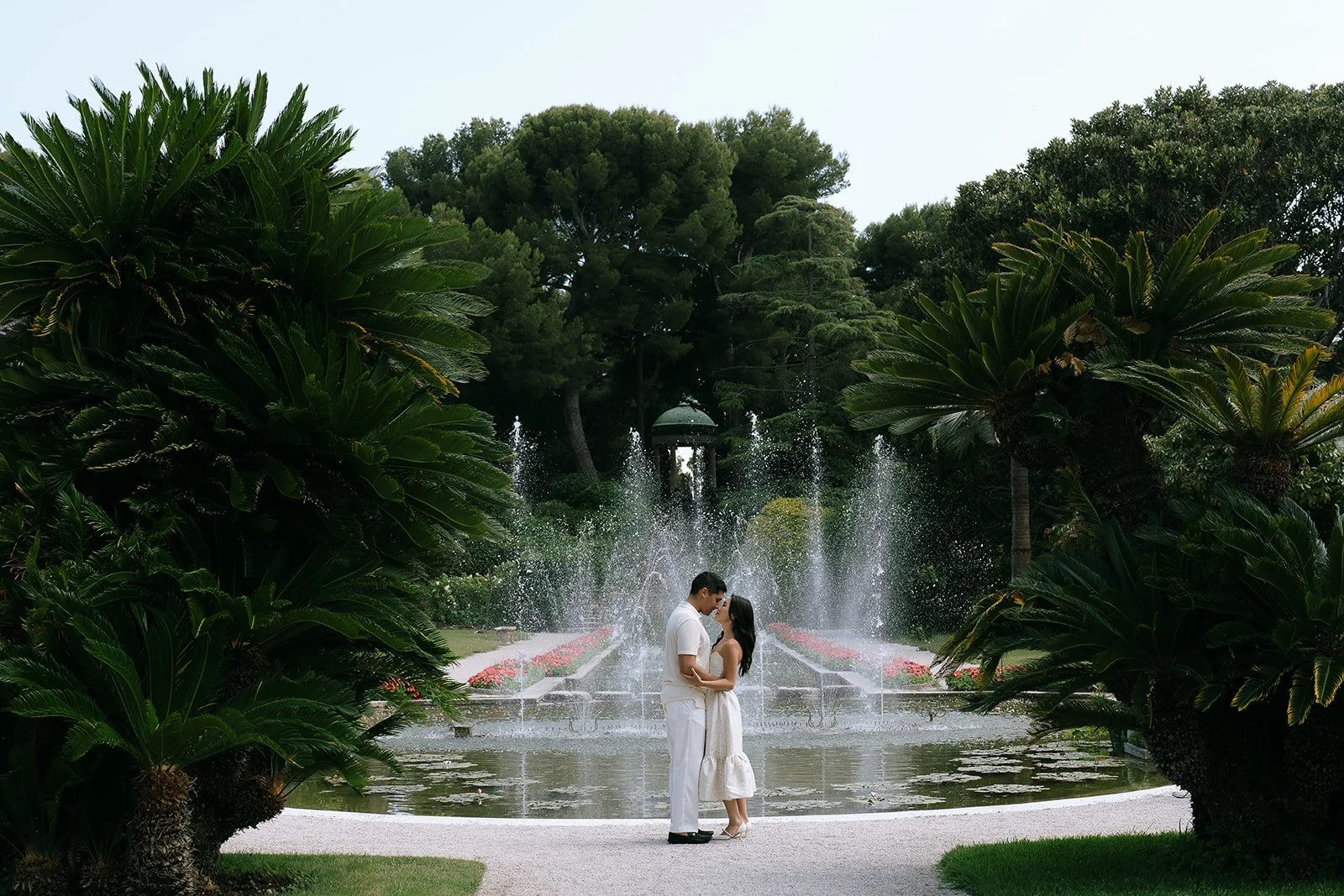 Couple kiss in front of a flowing fountain and lush greenery in the French Garden of the Villa Ephrussi during their destination engagement photoshoot on the South of France