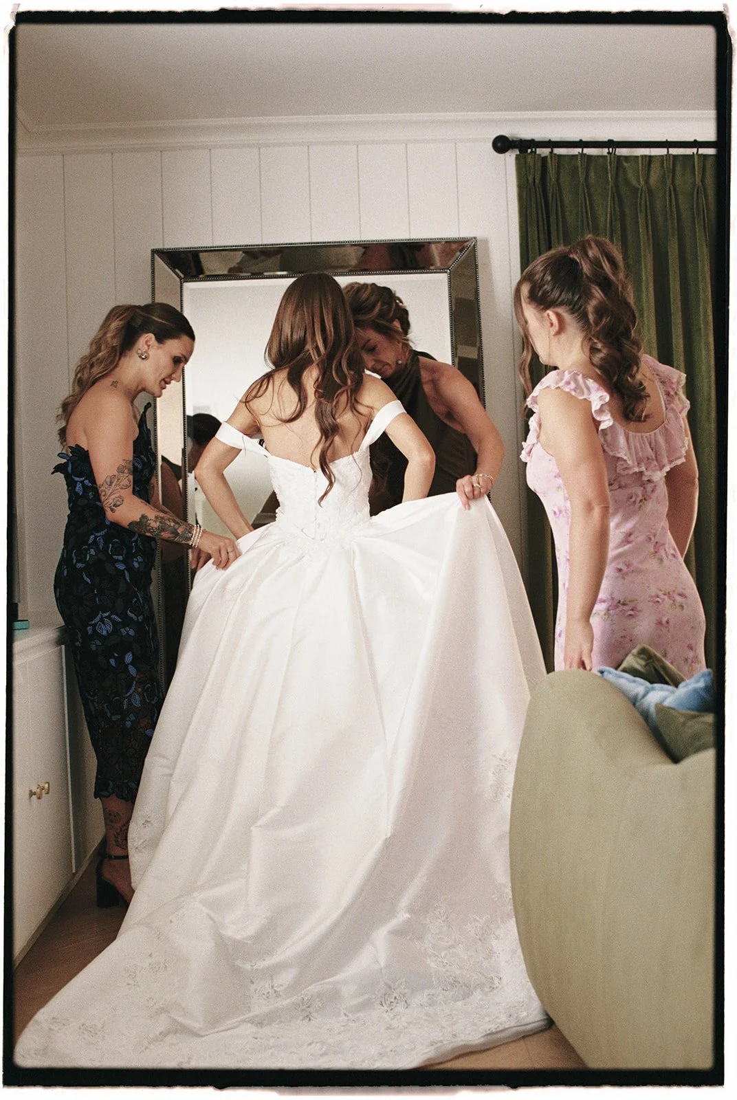  The bride putting on her   Archive Bridal   wedding gown with the help of the Mother of the Bride and family. 35 mm film. 