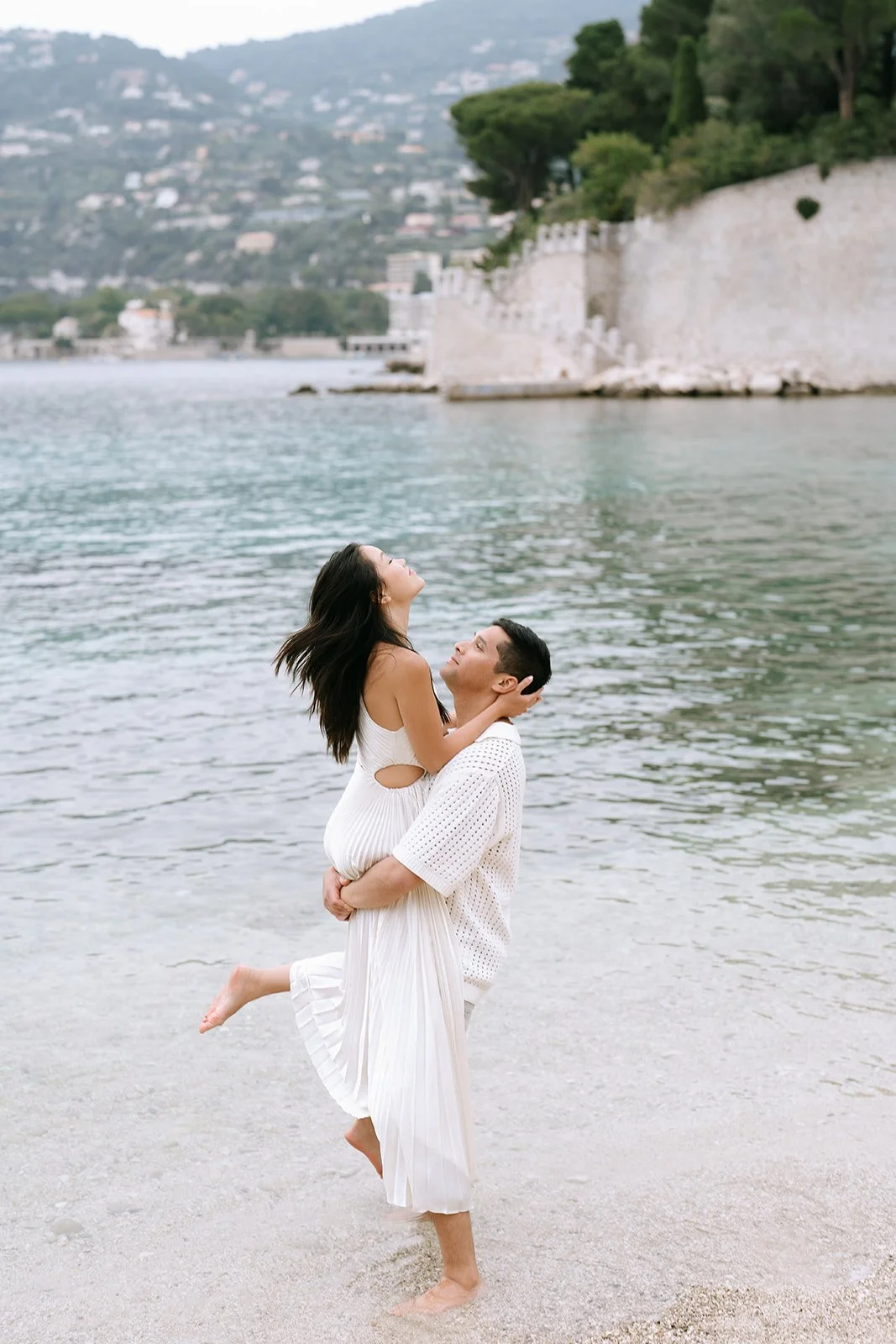 Soon to be groom holds his soon to be bride in the air on the Mediterranean coast during a beach engagement photoshoot