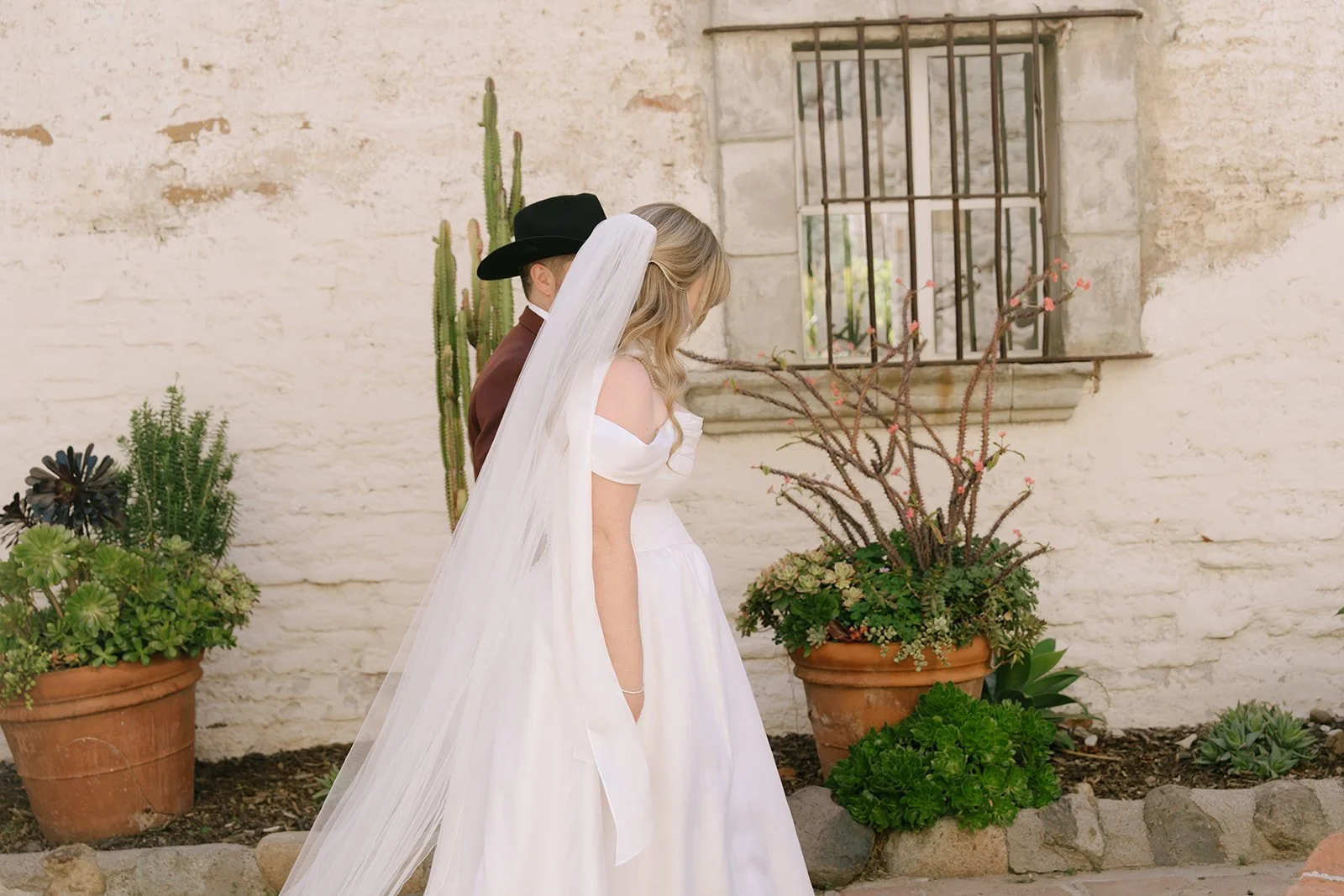 Bride and groom walk holding hands at the Mission San Juan Capistrano.