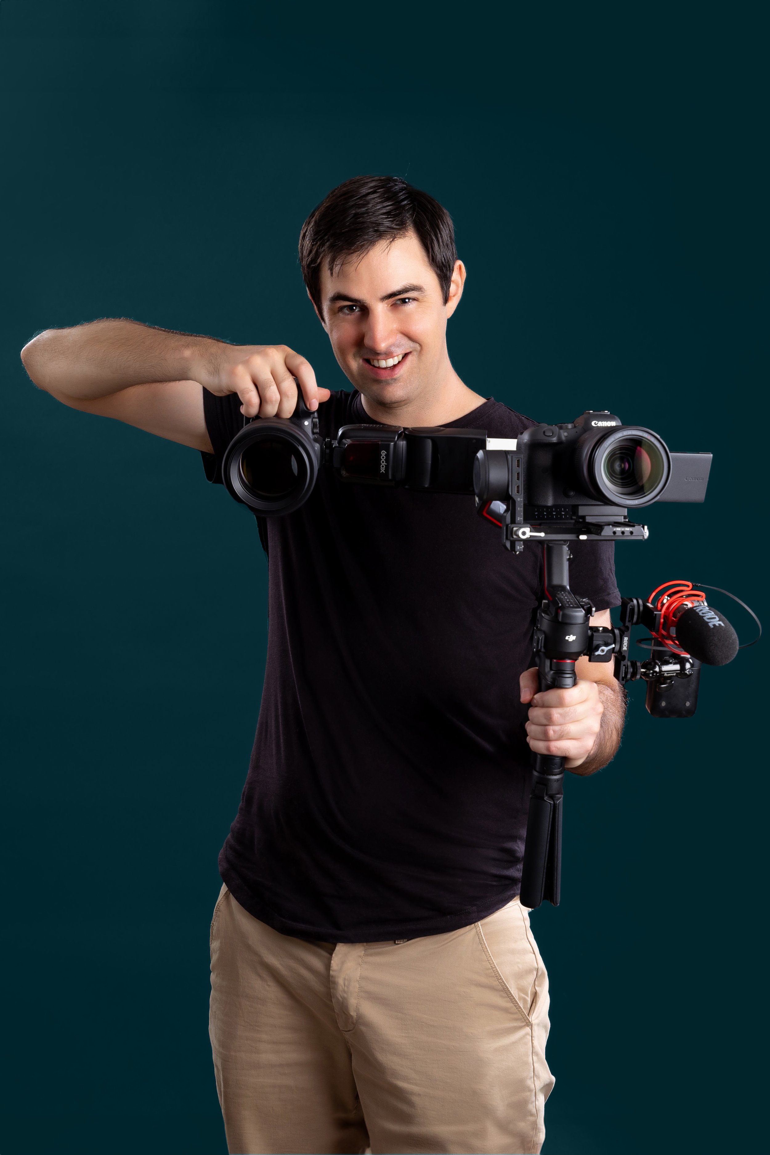 Portrait of videographer and photographer Brent holding a video camera against a dark teal background.