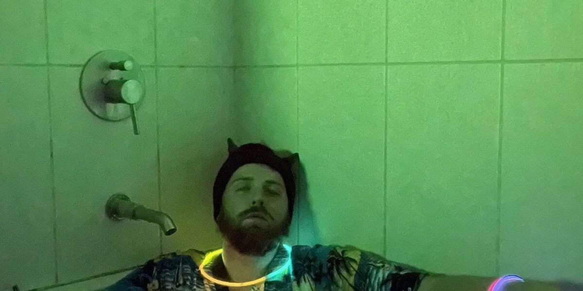 A person sitting prone in a shower recess lighted green. Exhausted, glow stick necklace and bracelet