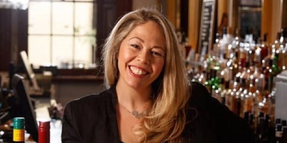 Anna Thomas, long blonde hair, black top, silver necklace, smiling at the camera